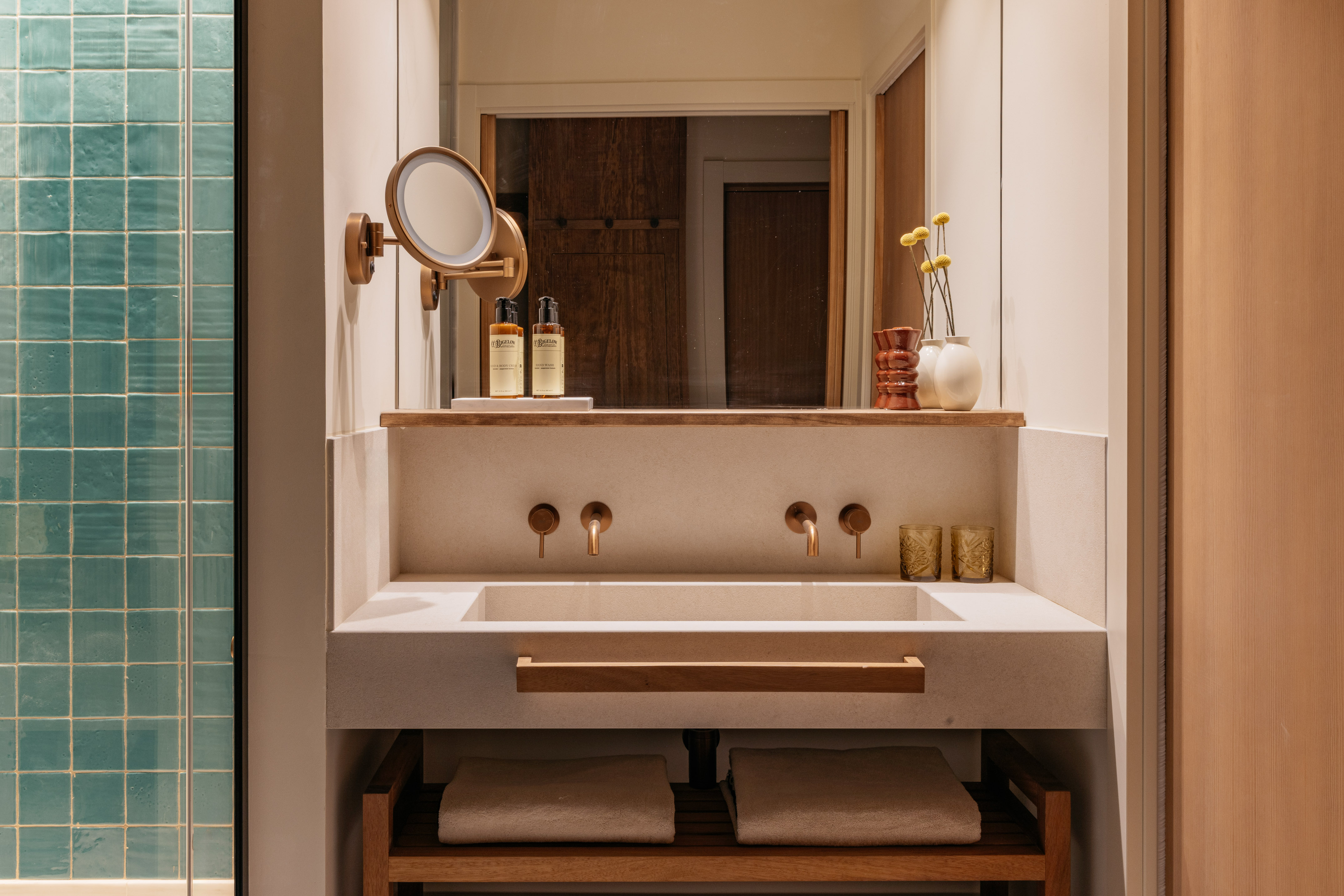Modern bathroom vanity with concrete sink, bronze fixtures, and teal shower tiles.