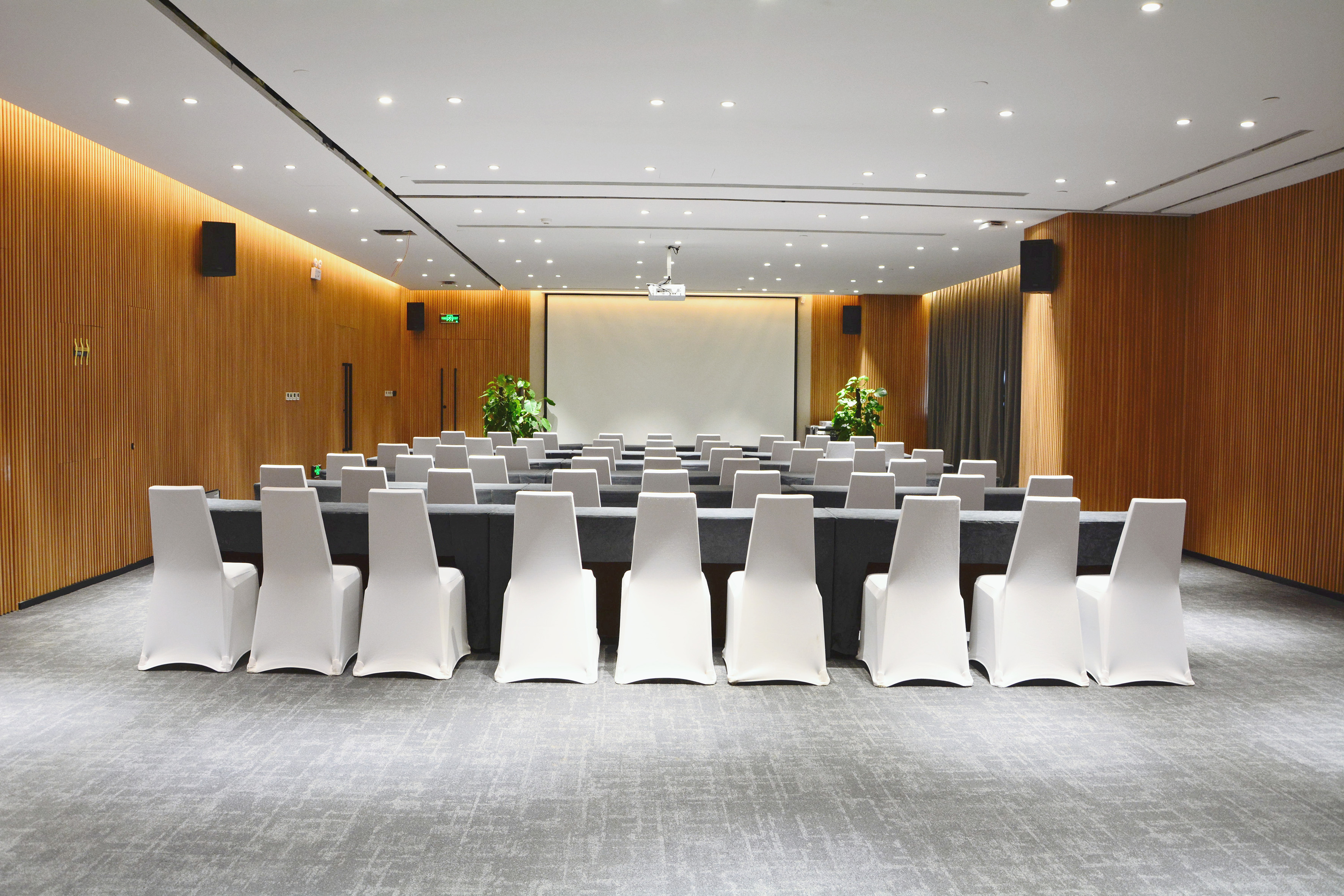 Modern conference room with white chairs, tables, and projection screen.