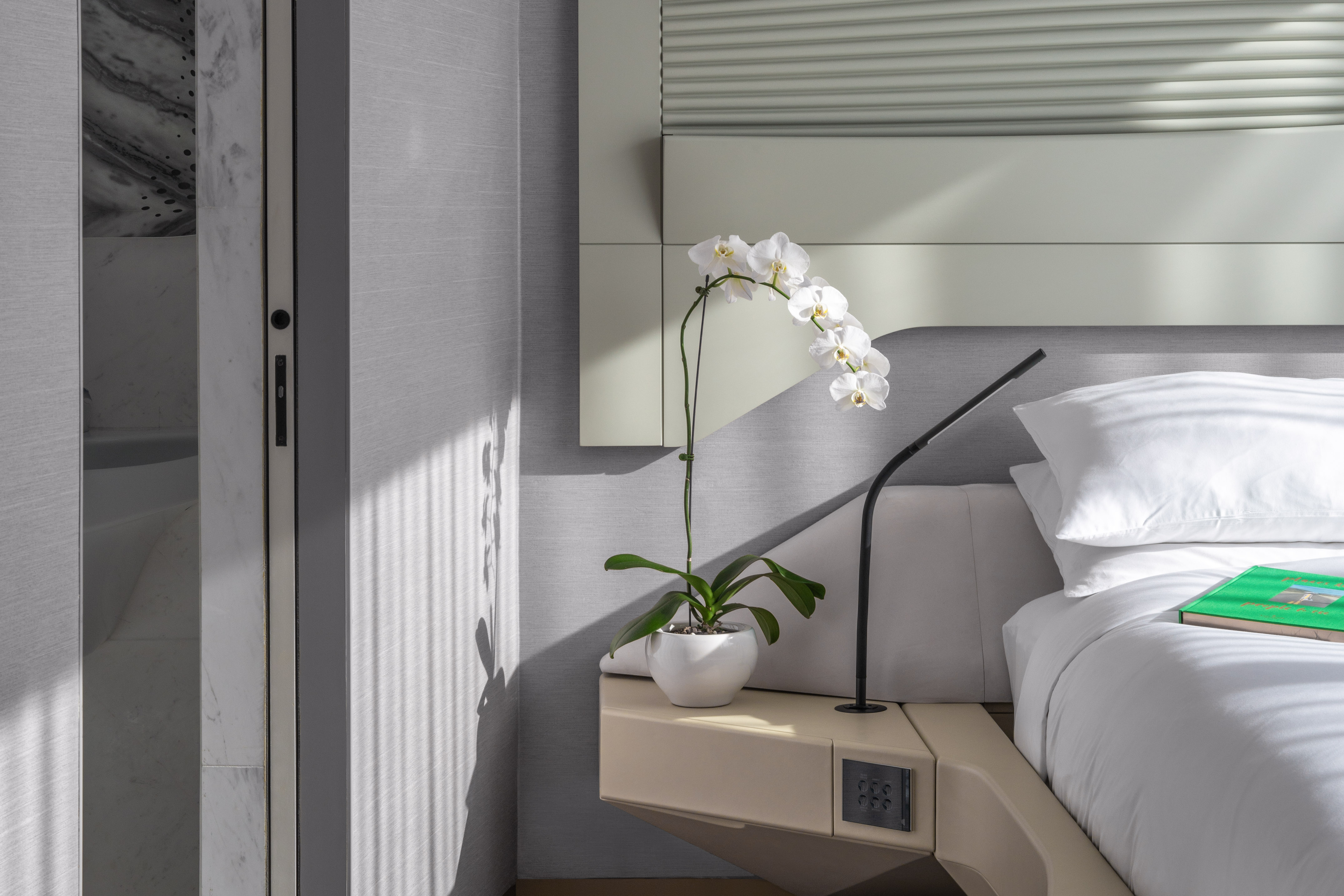 Elegant bedroom interior: white orchid, modern bedside table, white bedding.