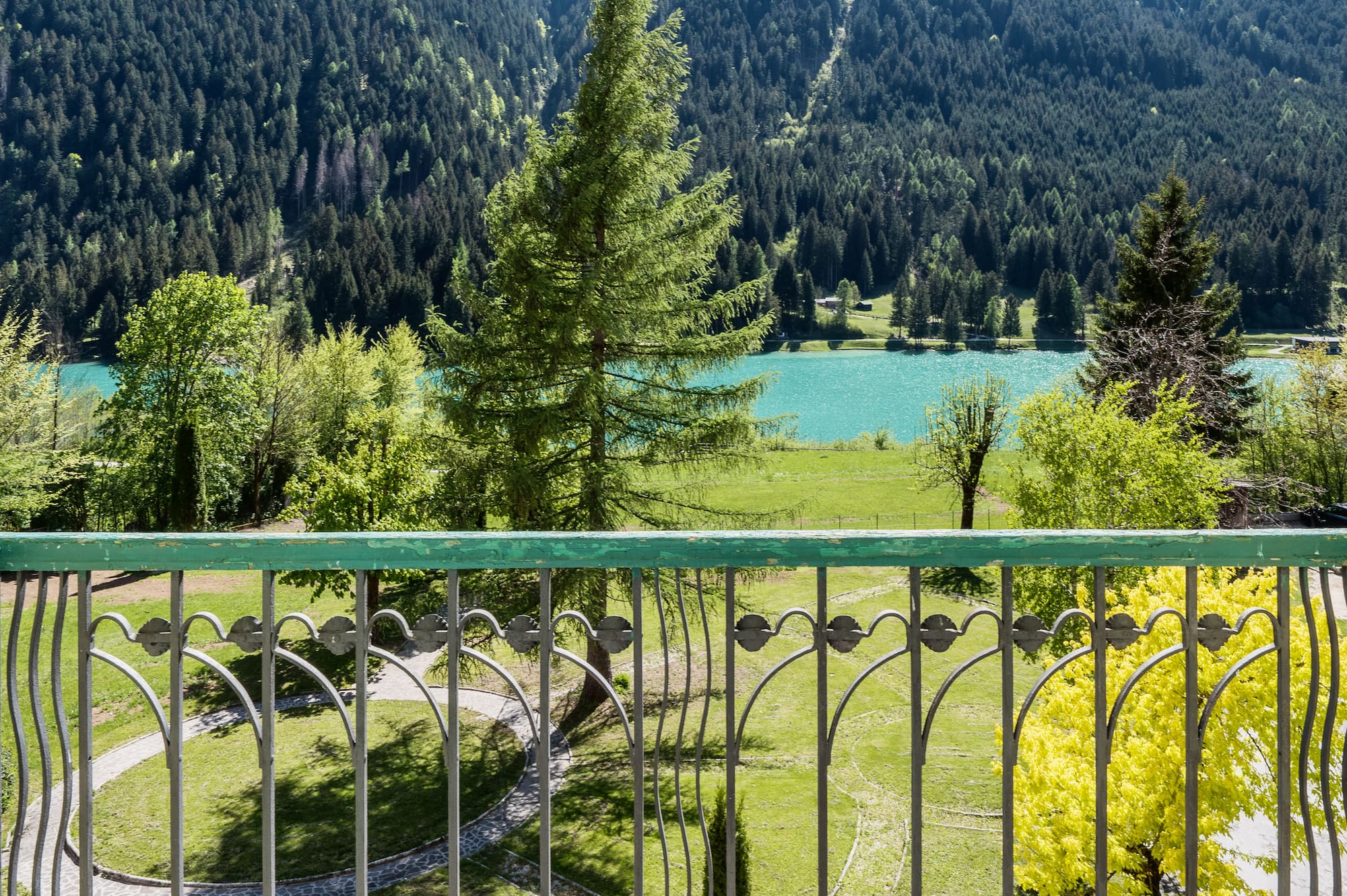 Balcony view over turquoise mountain lake, dense forest, and green park.
