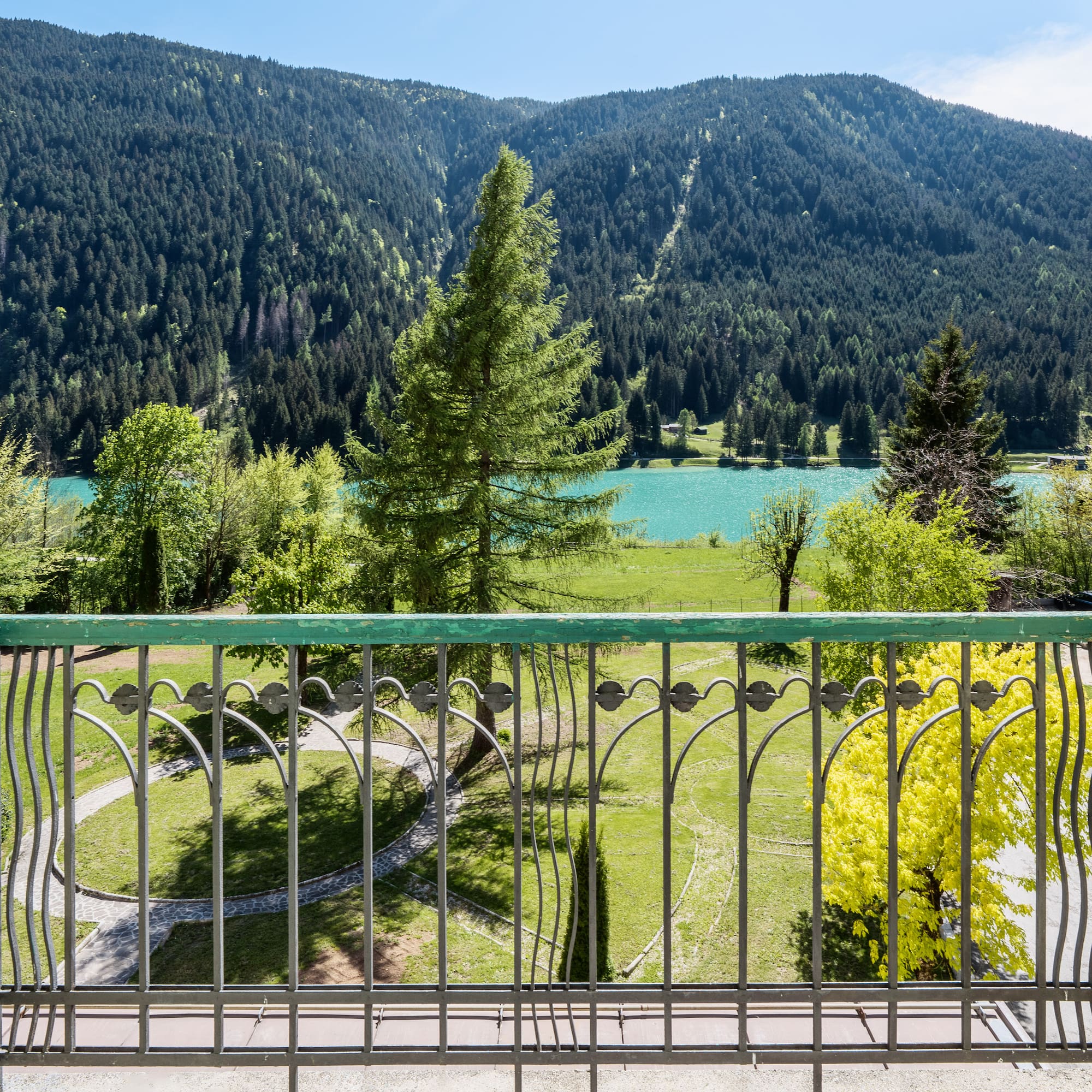 Balcony view over turquoise mountain lake, dense forest, and green park.