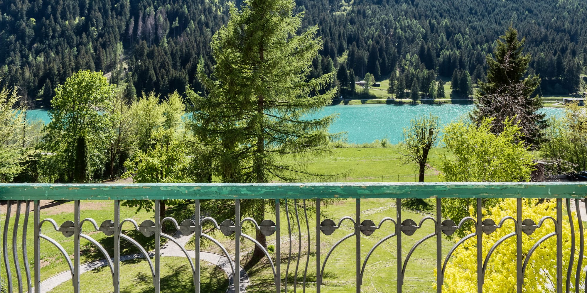 Balcony view over turquoise mountain lake, dense forest, and green park.