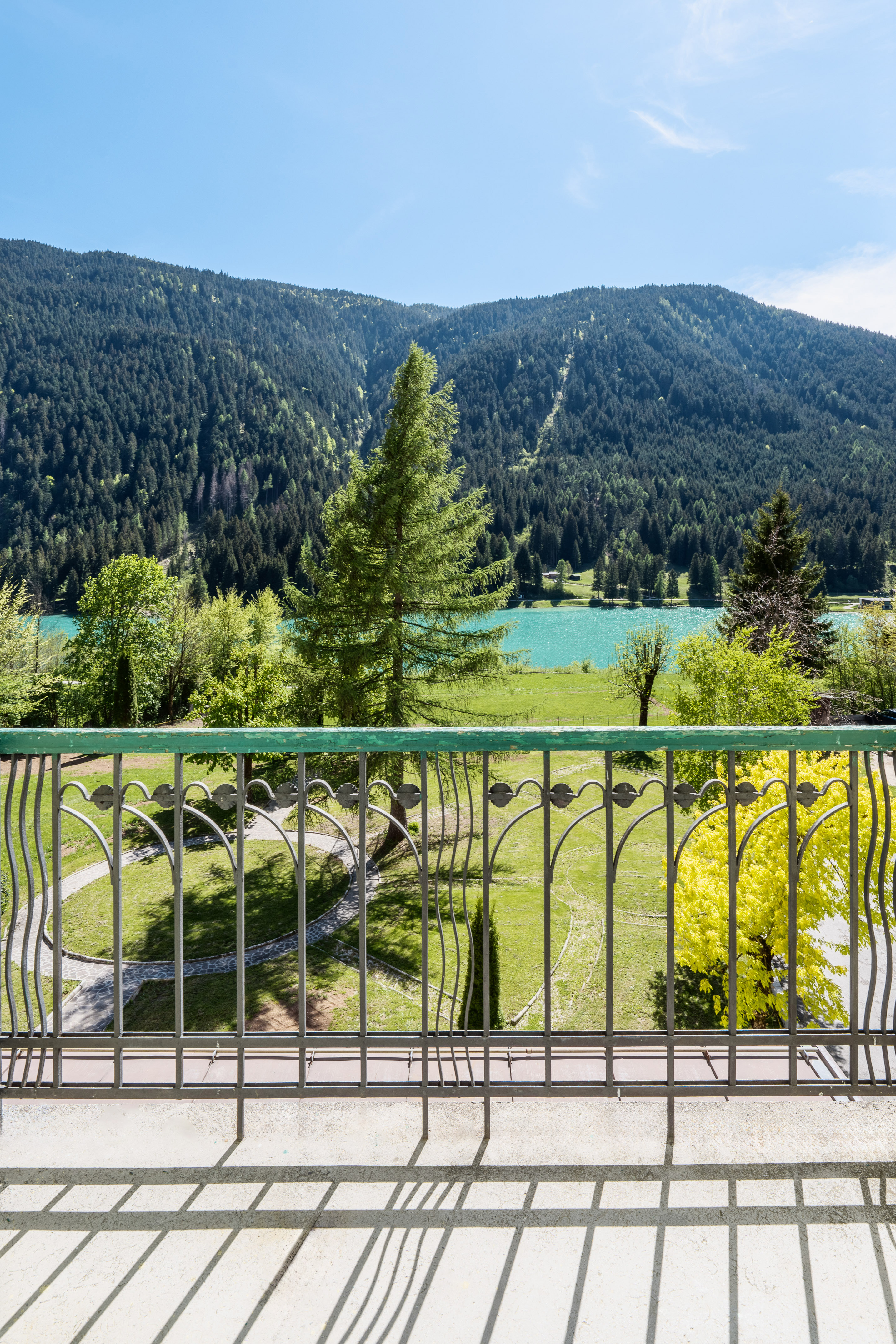 Balcony view over turquoise mountain lake, dense forest, and green park.