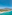 Aerial view of turquoise sea, sandy beach, coastal resort, mountains, and pier.