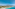 Aerial view of turquoise sea, sandy beach, coastal resort, mountains, and pier.