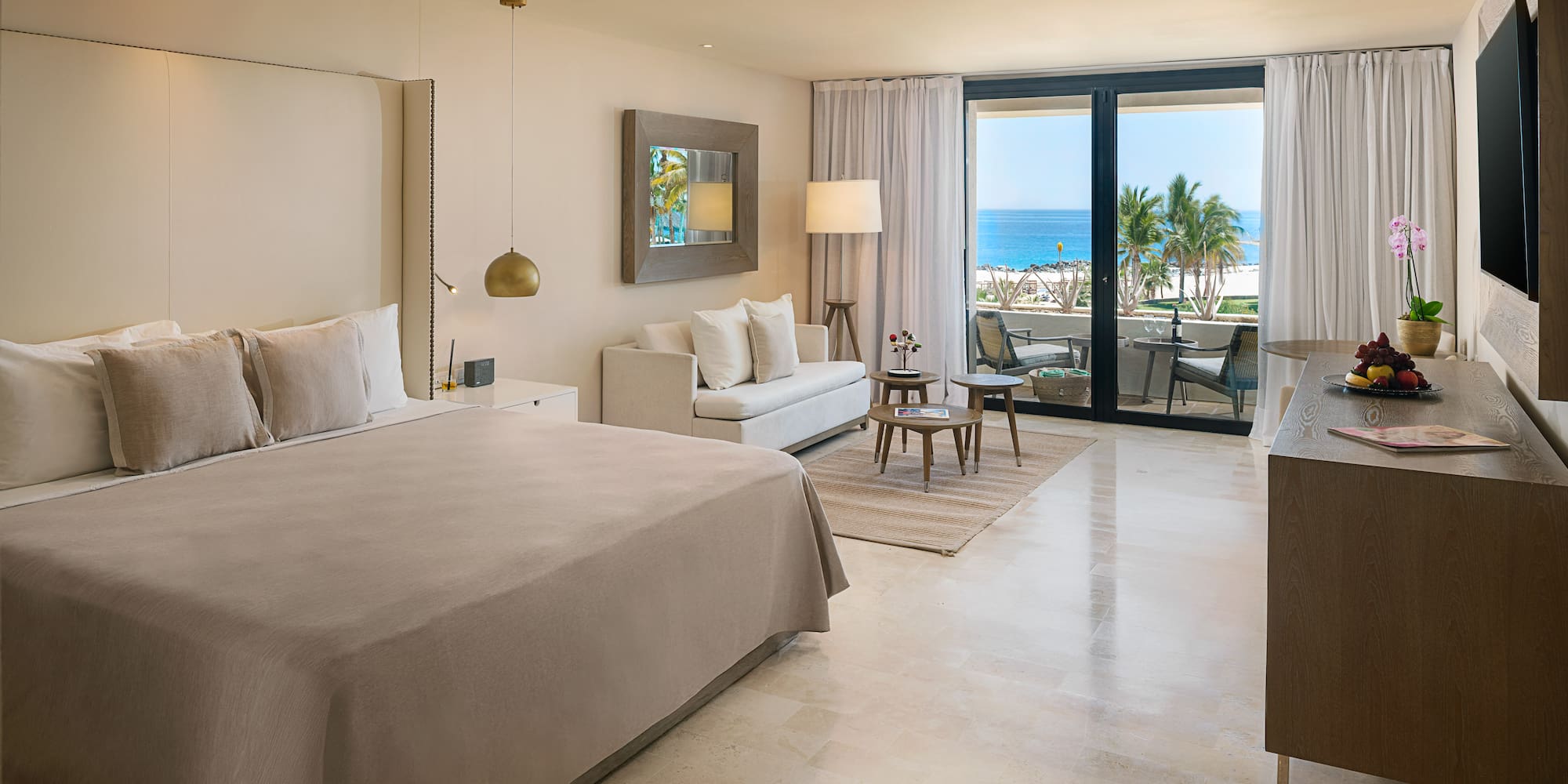 Luxury hotel room with ocean view balcony, king bed, and modern decor.