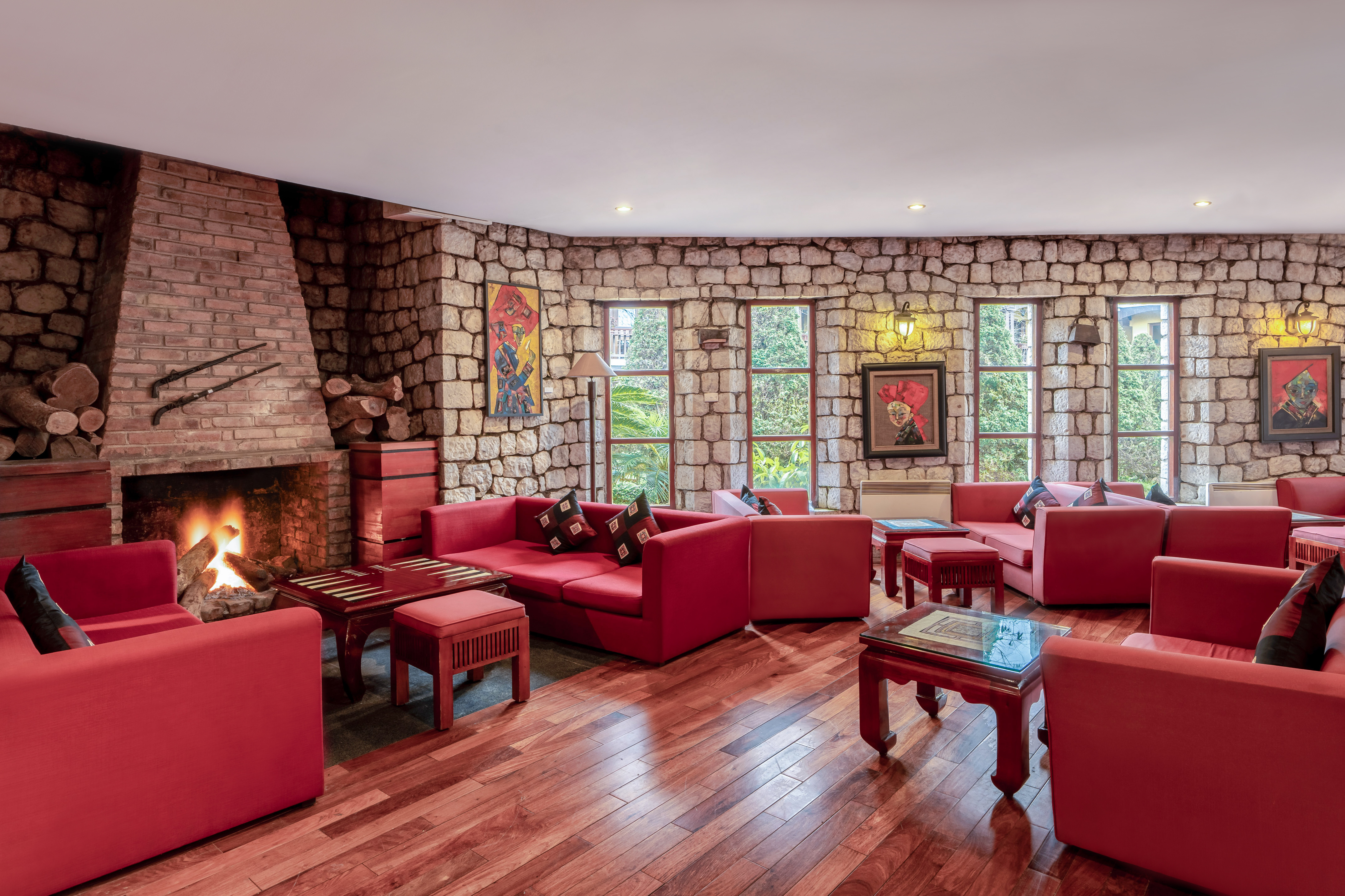 Cozy hotel lounge with stone walls, a burning fireplace, and red sofas.