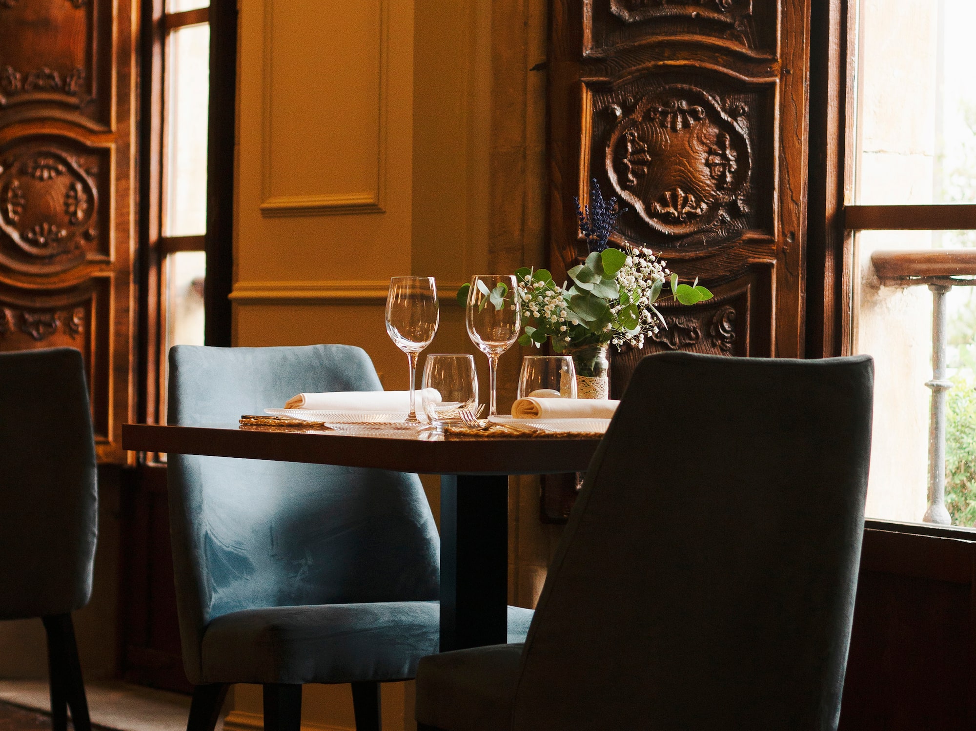 a table with wine glasses and chairs in a room with a window