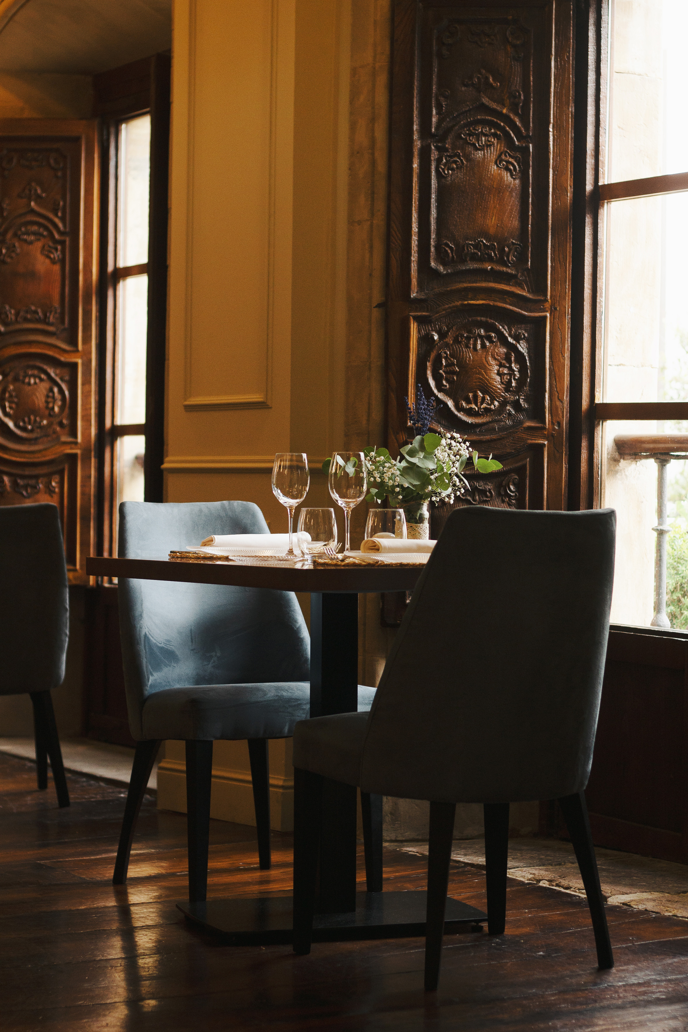 a table with wine glasses and chairs in a room with a window