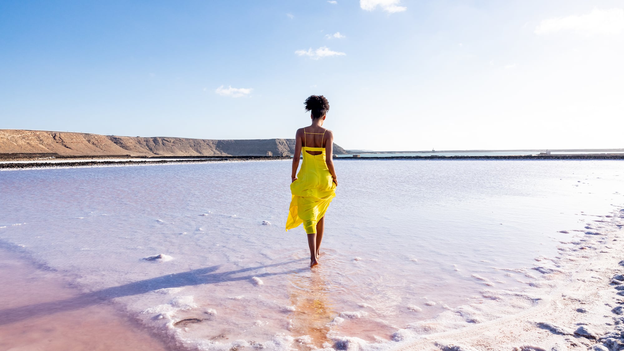 a woman in a yellow dress walking in water