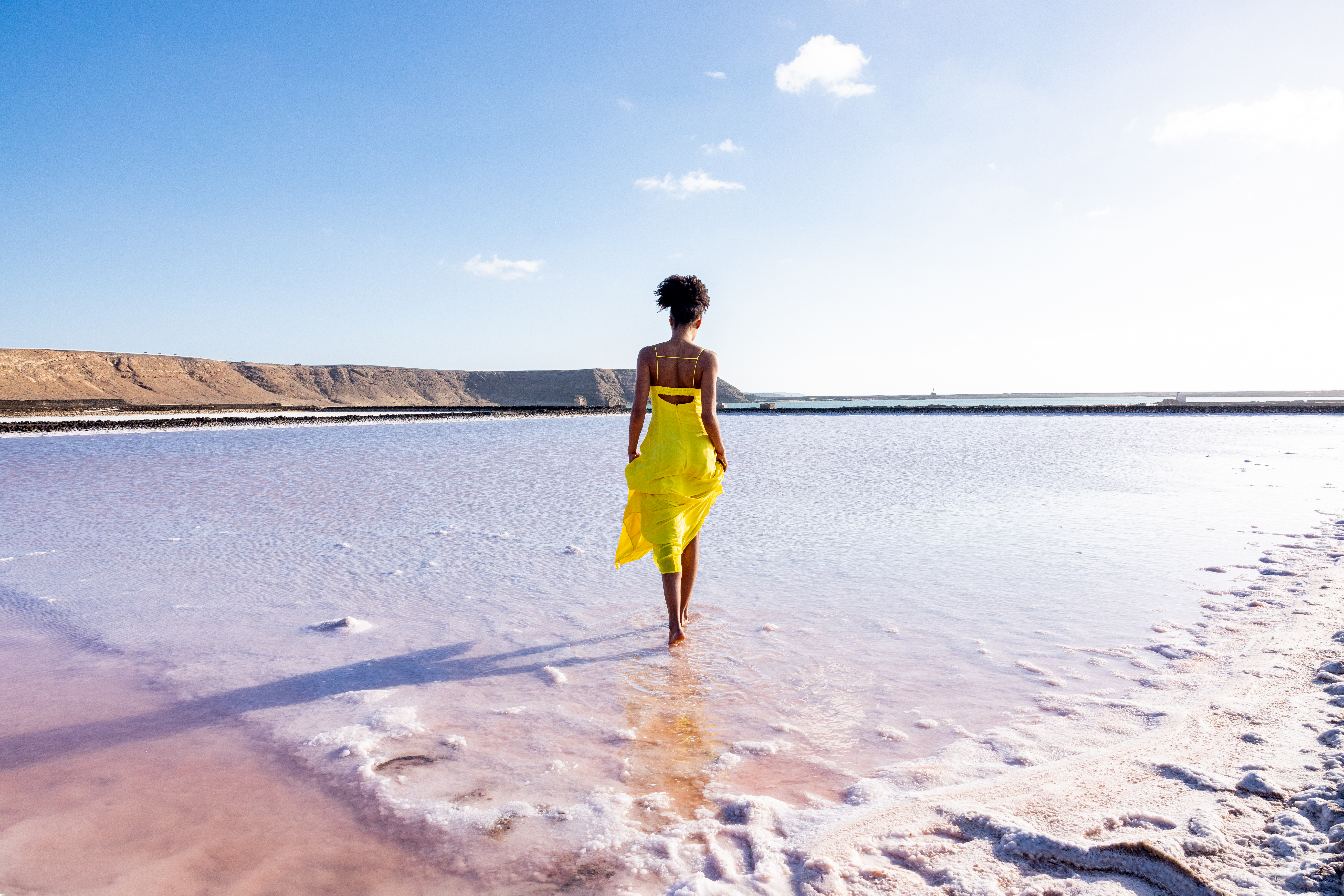 a woman in a yellow dress walking in water
