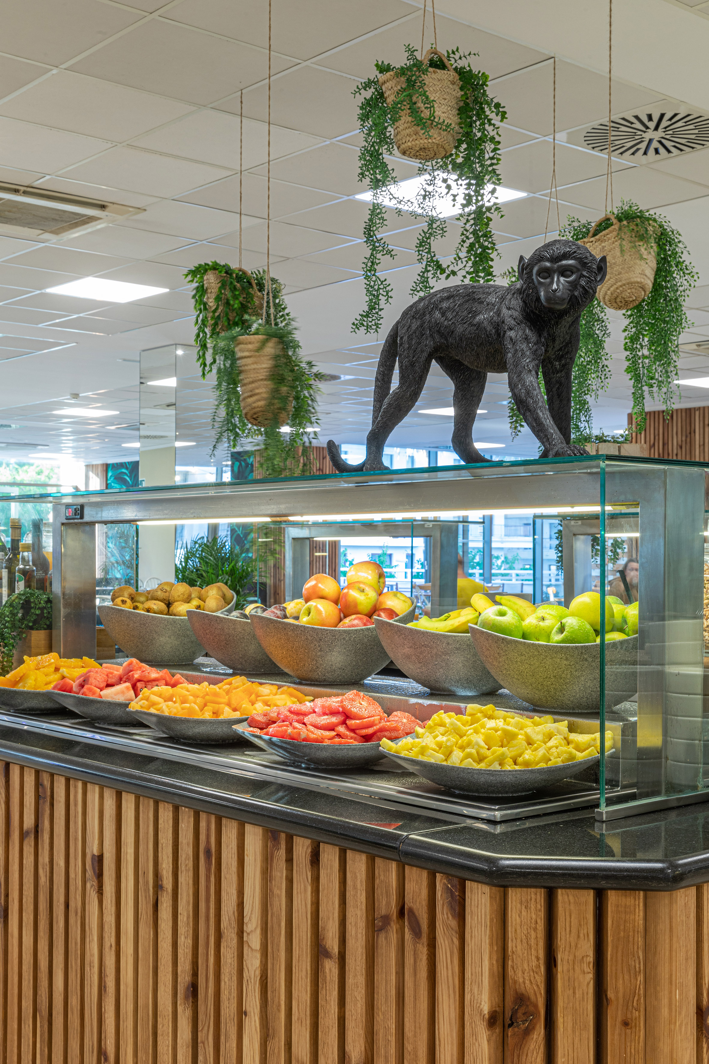 Fresh fruit buffet with black monkey statue, kiwi, apples, bananas, pineapple.