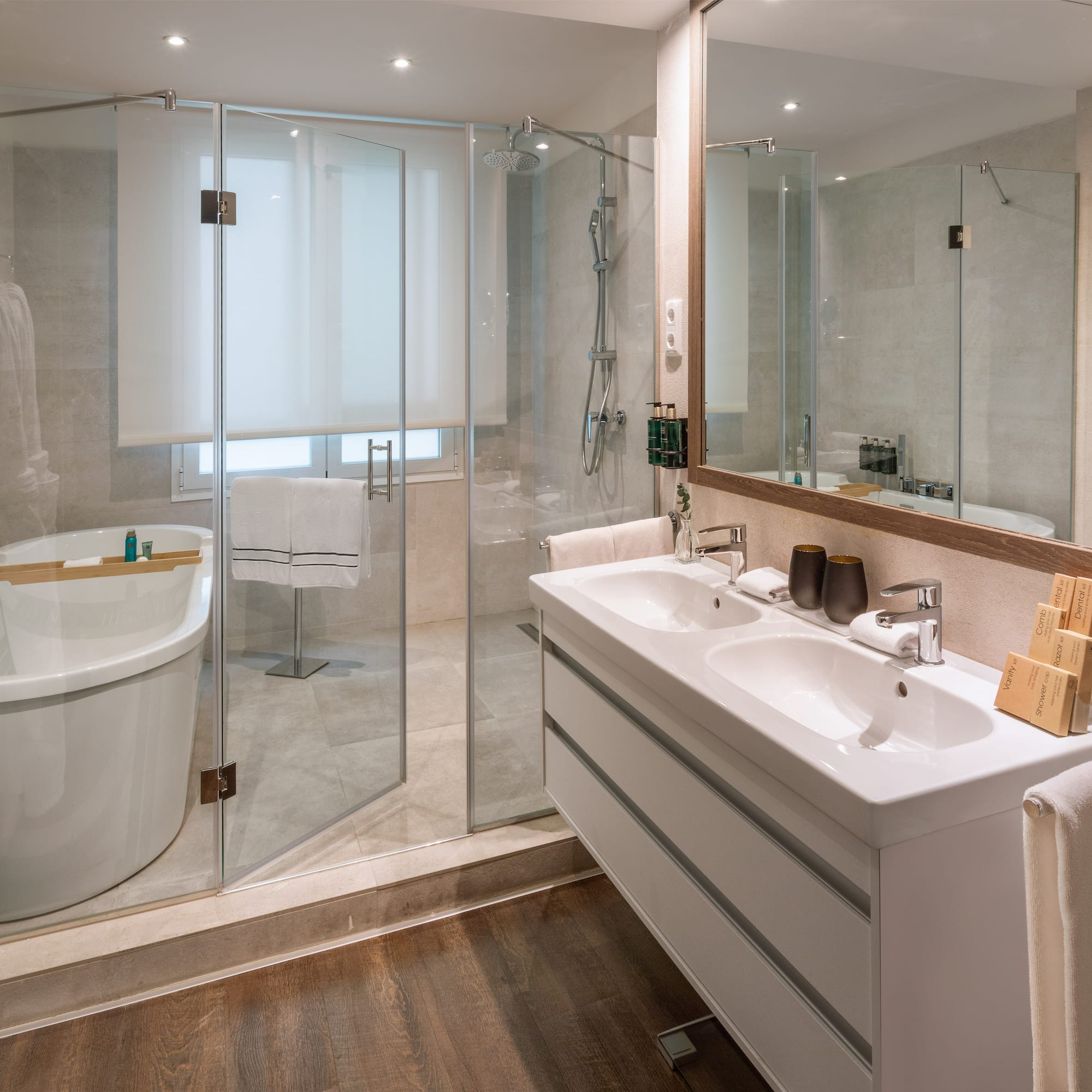Modern bathroom: glass shower, freestanding tub, double vanity, wooden floor.