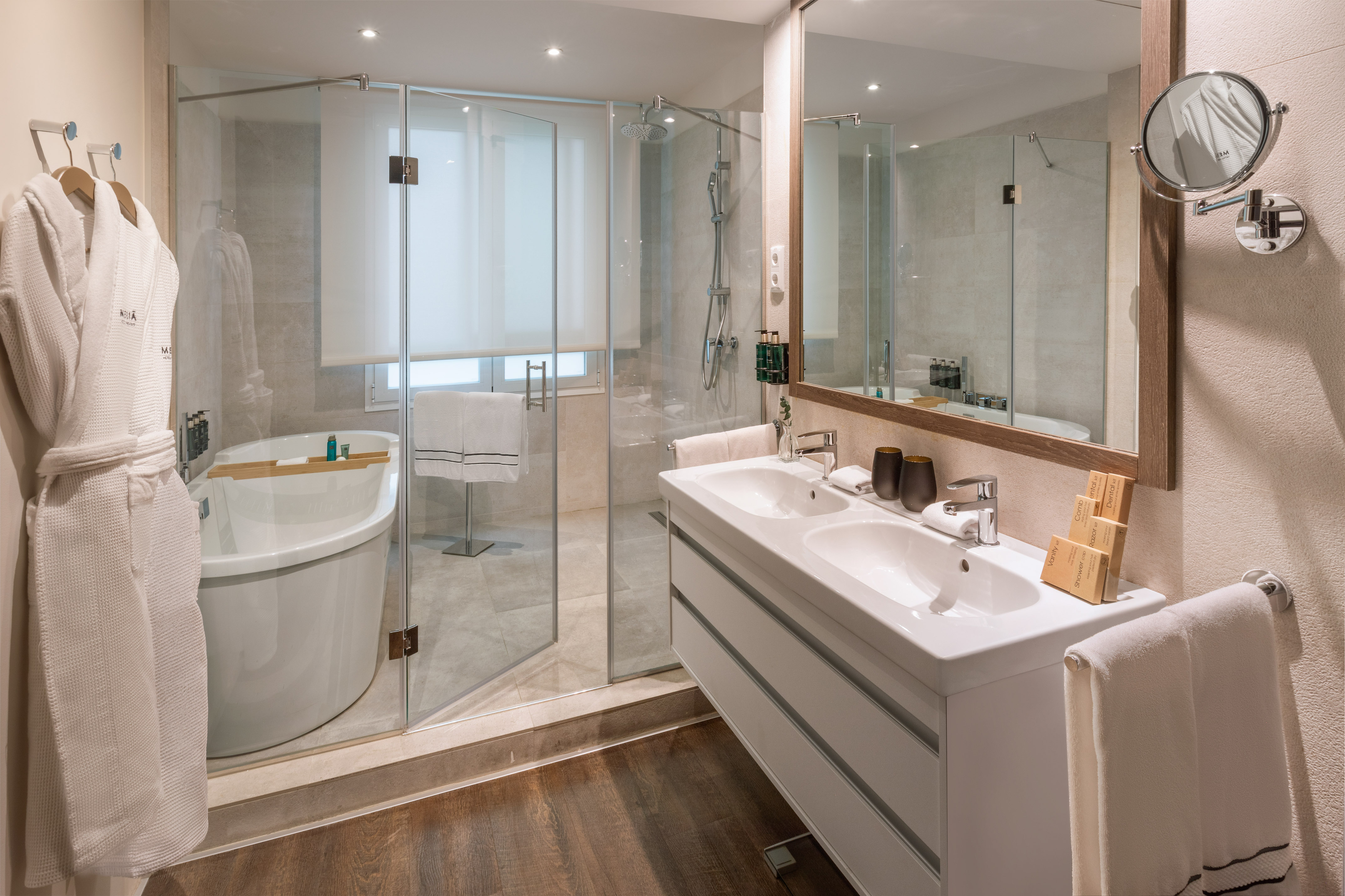 Modern bathroom: glass shower, freestanding tub, double vanity, wooden floor.