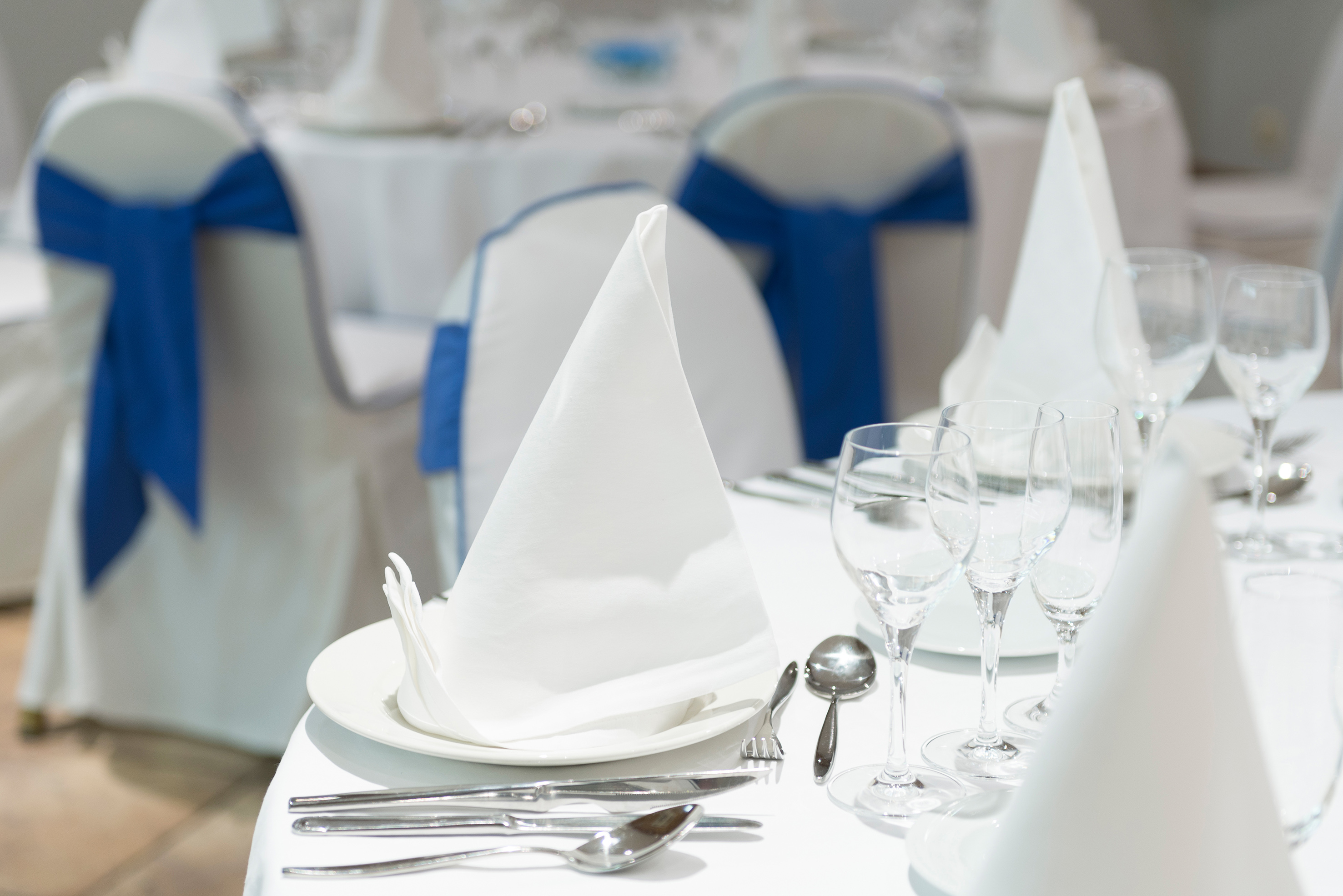Elegant white table setting with napkin, cutlery, wine glasses, blue accents.