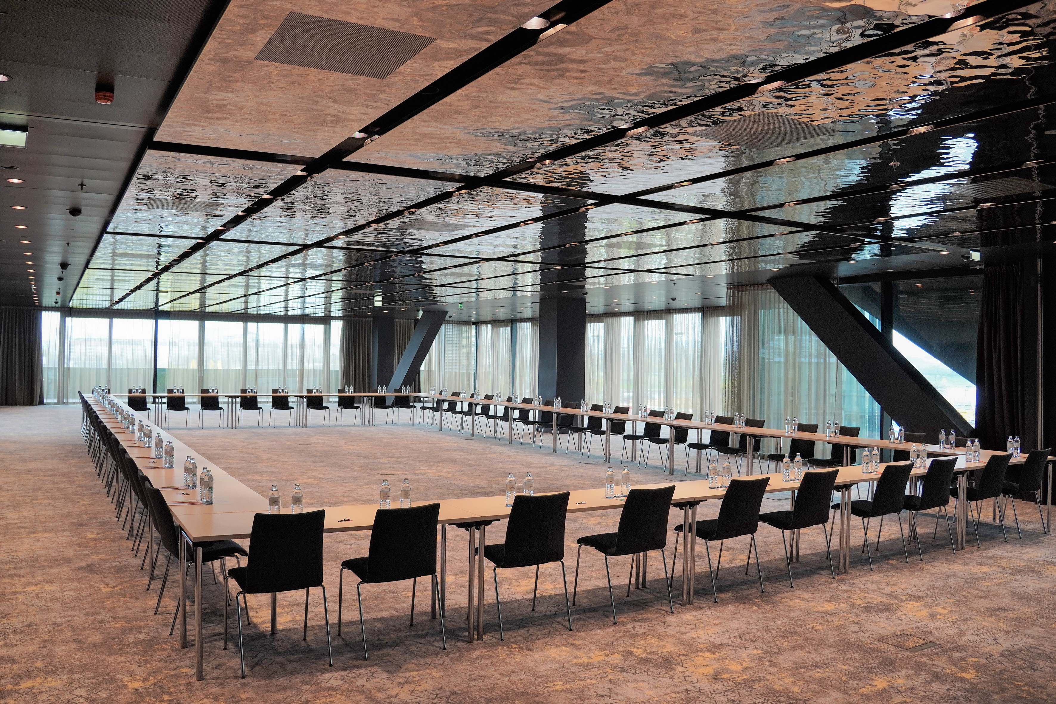 U-shape conference room setup with black chairs, water bottles, and reflective ceiling.