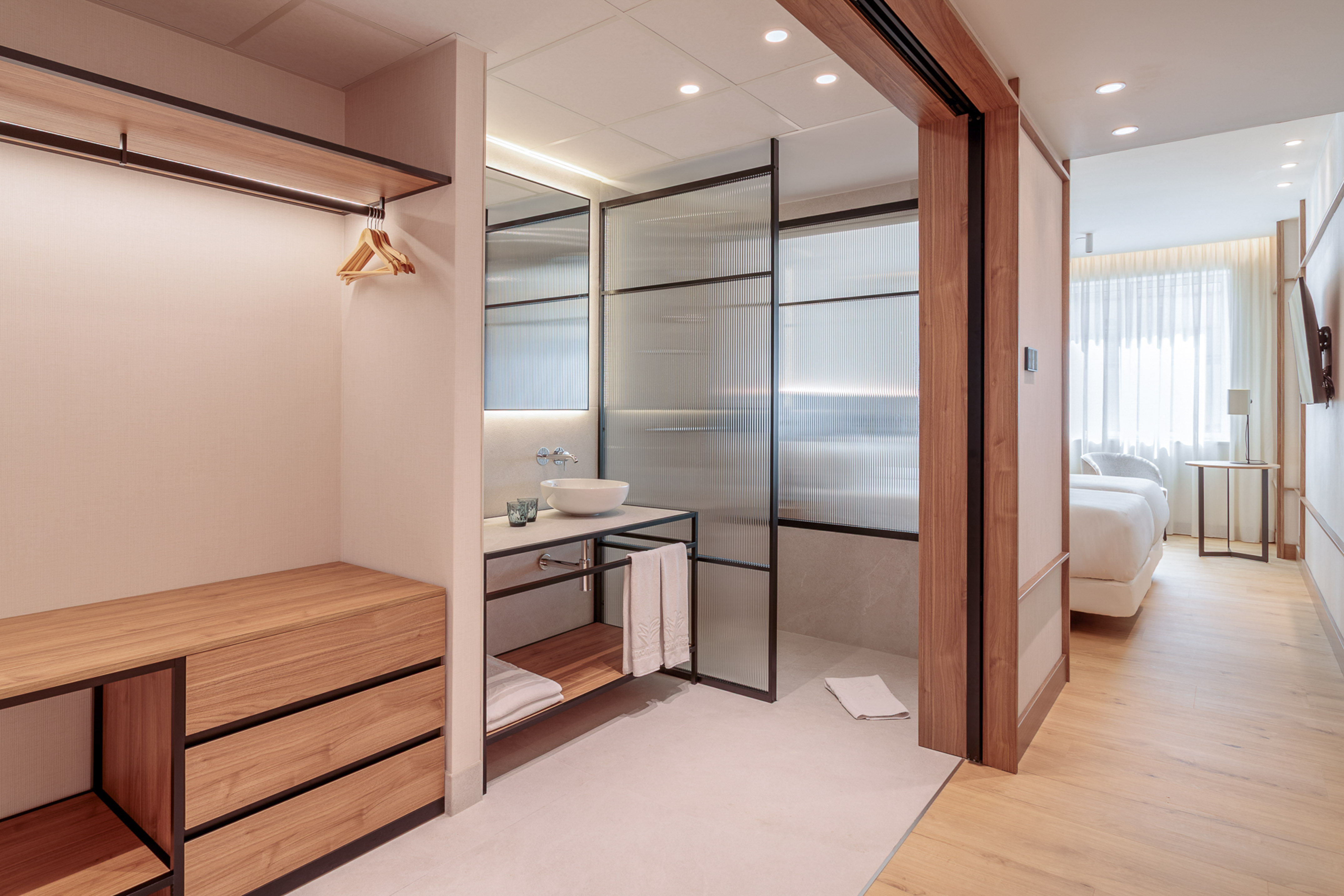 Modern hotel room with open closet, sleek bathroom, and bright bedroom area.