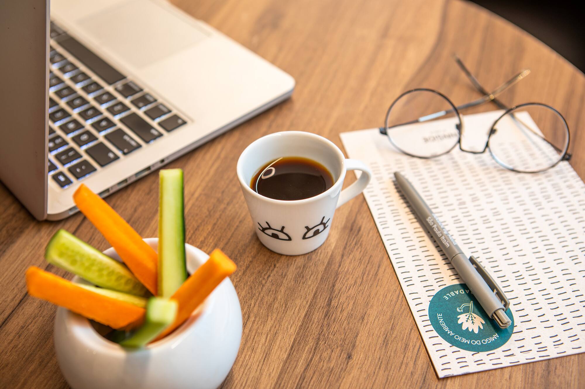 Home office desk: laptop, coffee, glasses, and veggie sticks.
