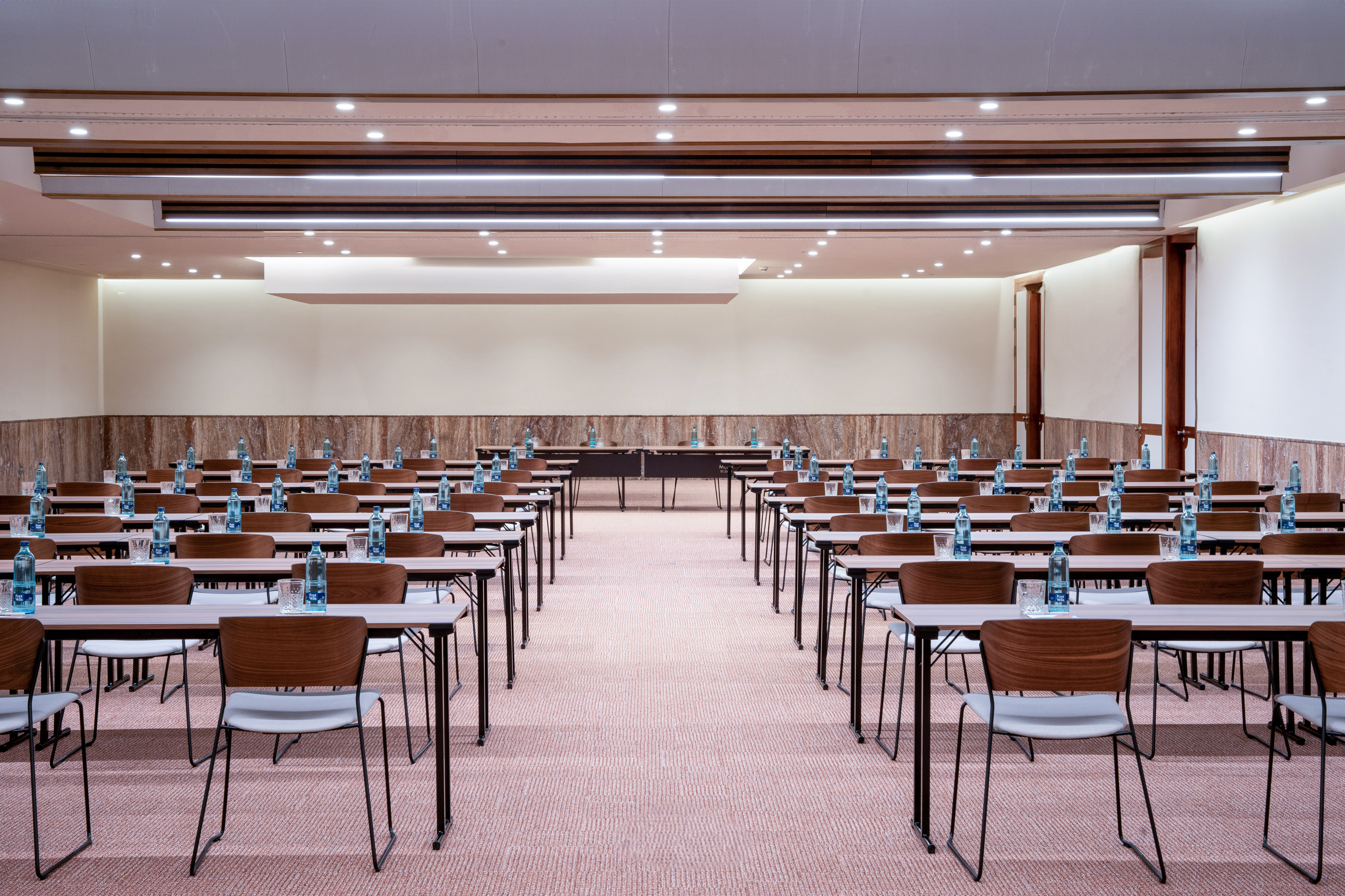Empty meeting room with classroom setup, rows of tables, chairs, water bottles.