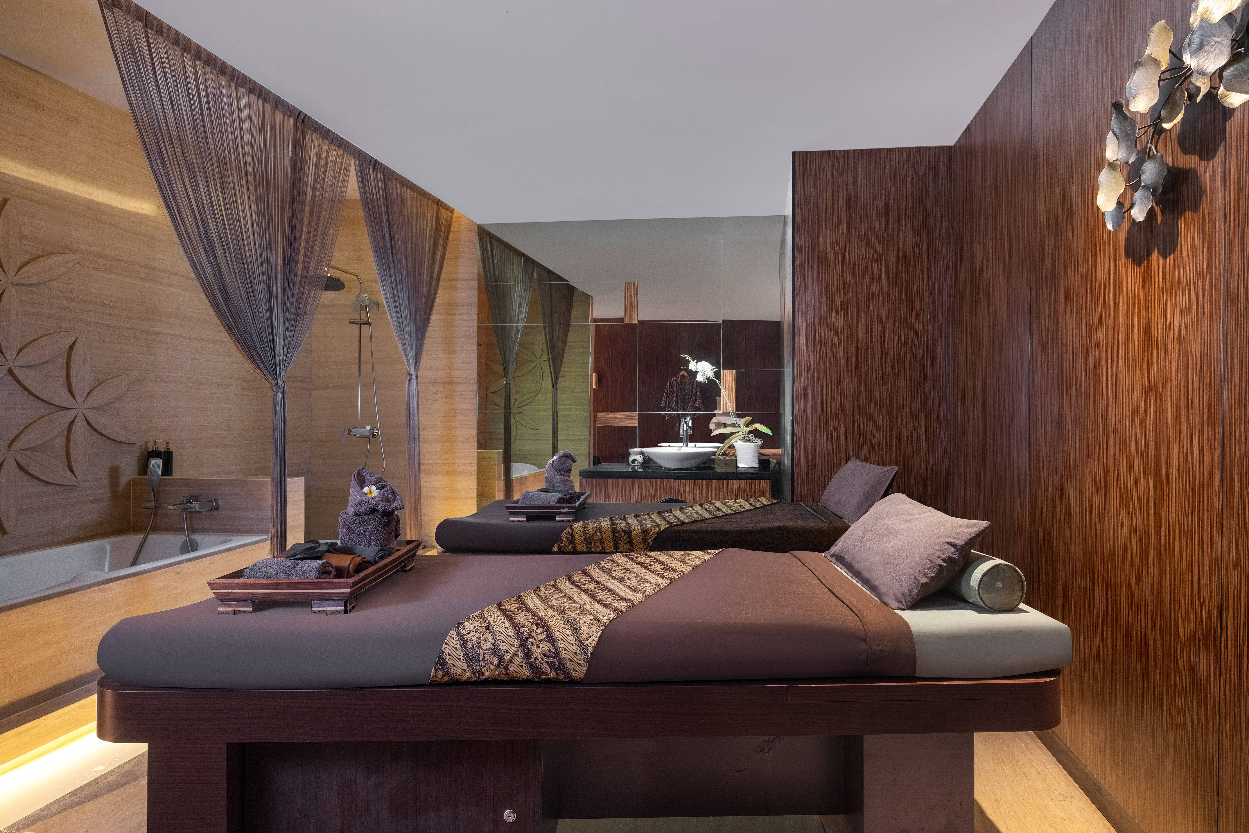 Luxury spa massage room with two beds, wooden accents, and a private bath.