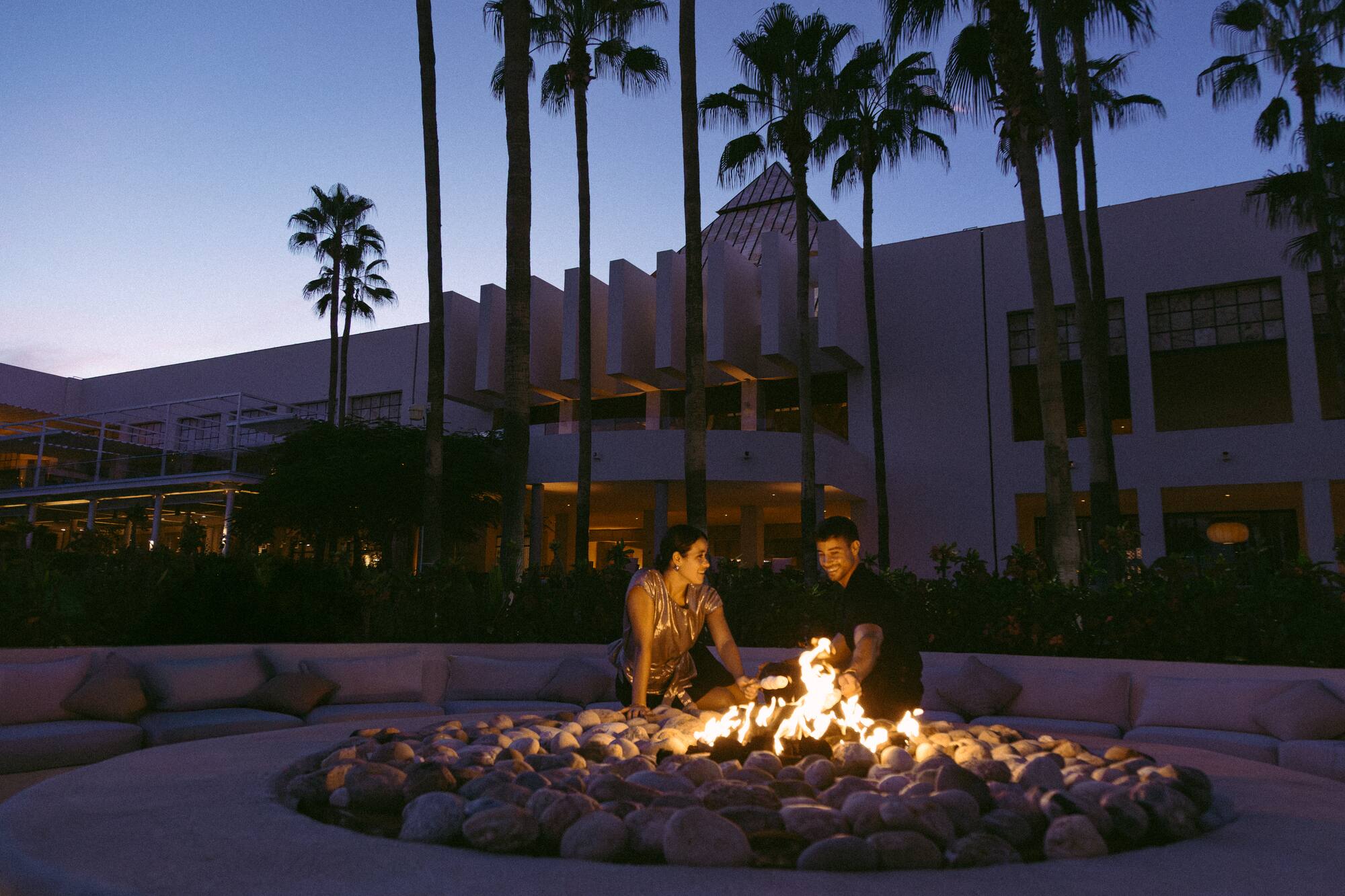 a man and woman standing around a fire pit