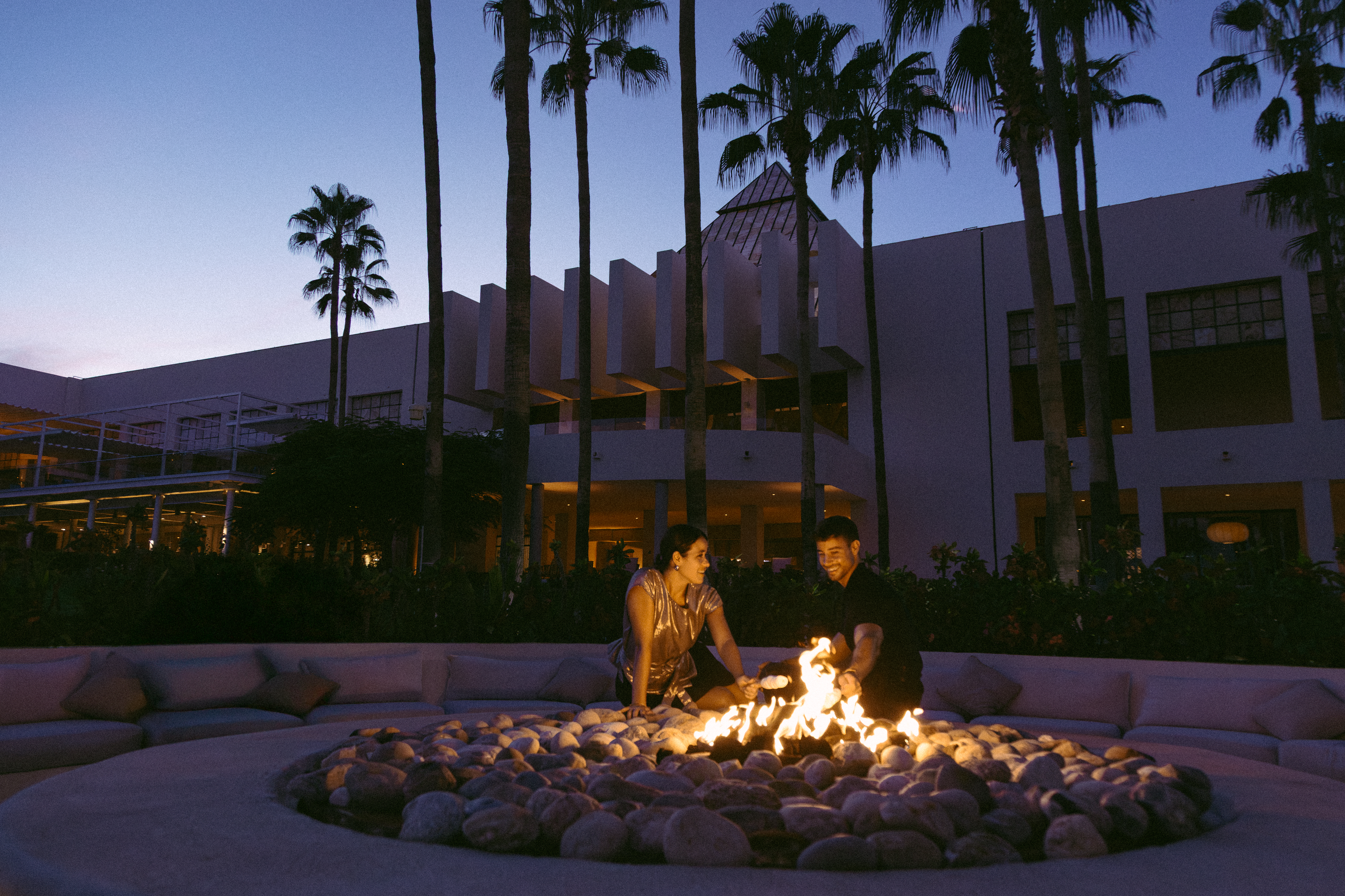 Couple by evening fire pit, luxury resort with palm trees.