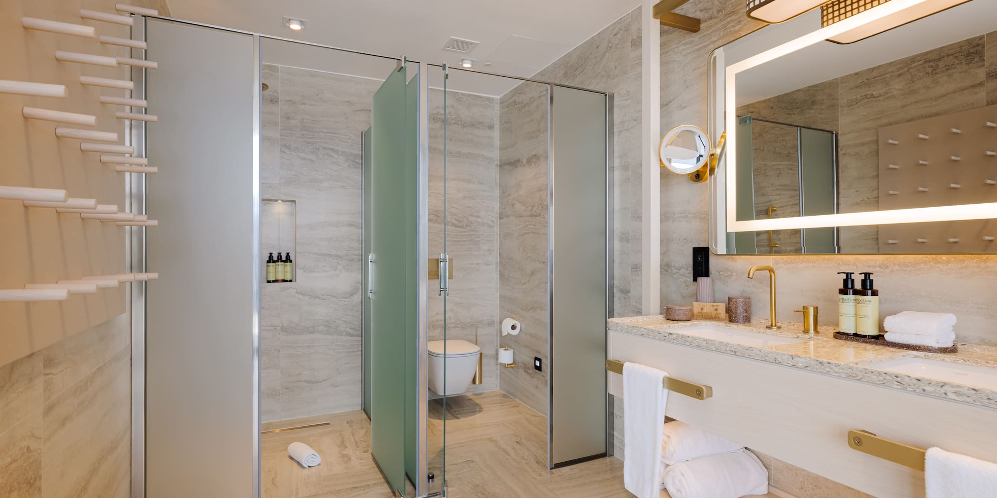 Modern luxury bathroom with gold fixtures, lighted mirror, and glass shower.