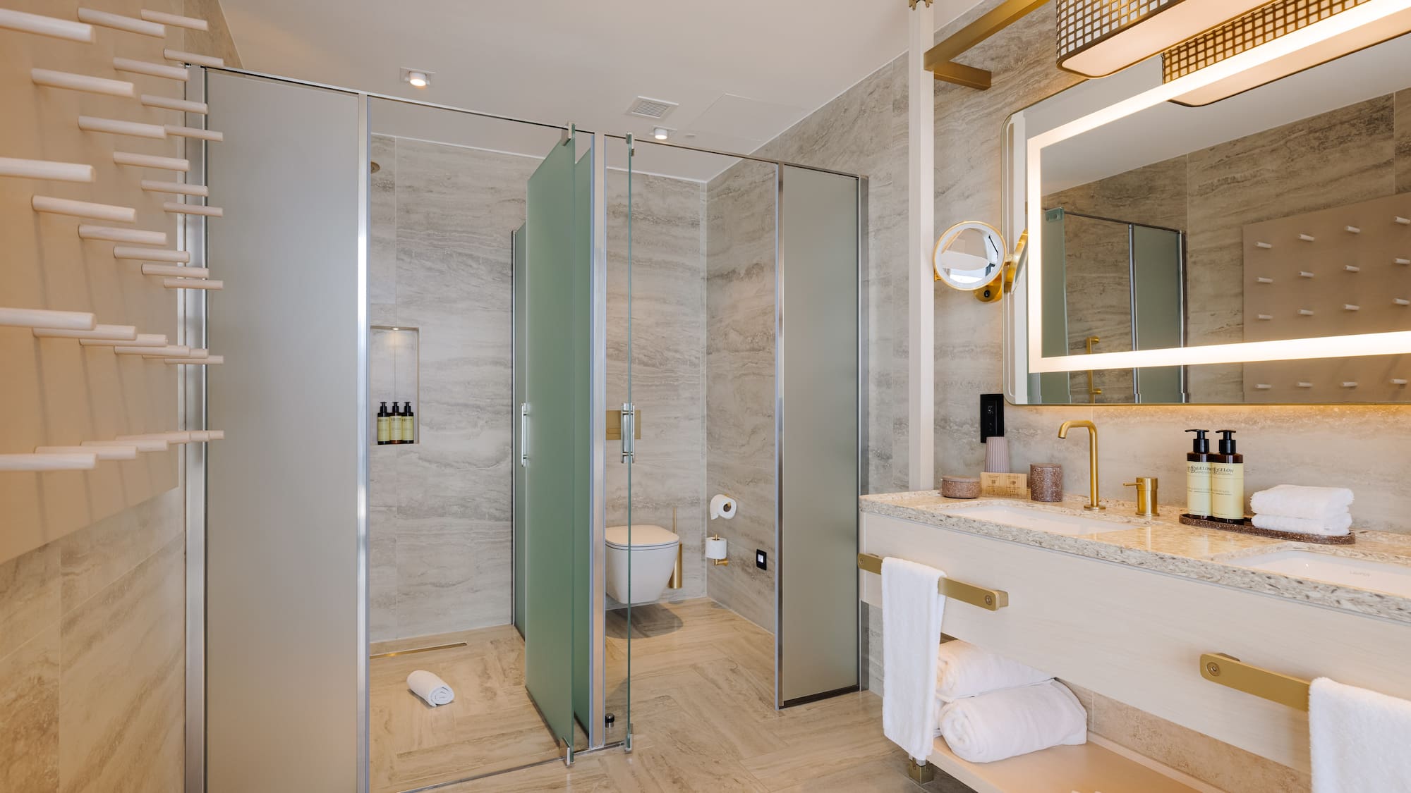 Modern luxury bathroom with gold fixtures, lighted mirror, and glass shower.