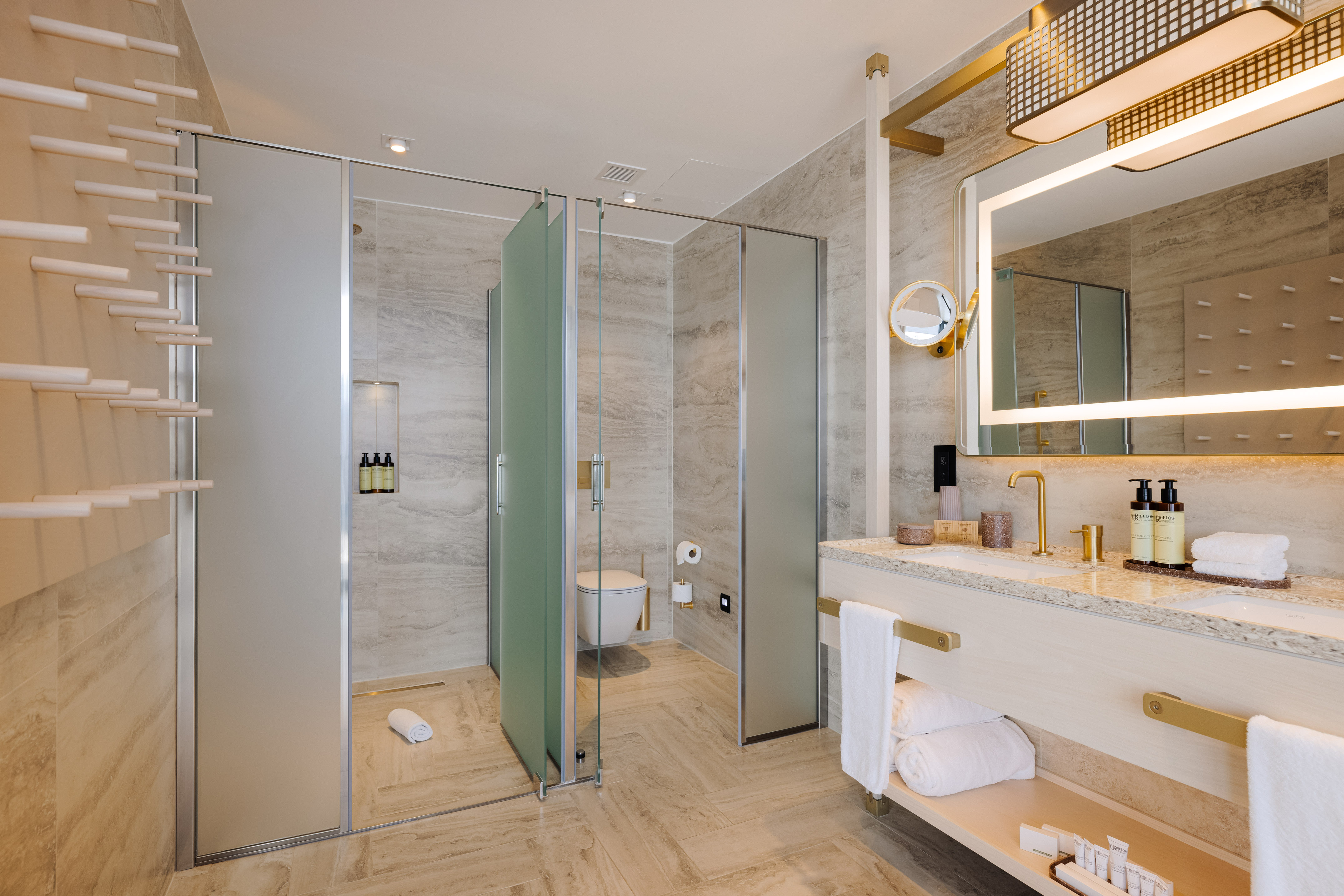 Modern luxury bathroom with gold fixtures, lighted mirror, and glass shower.