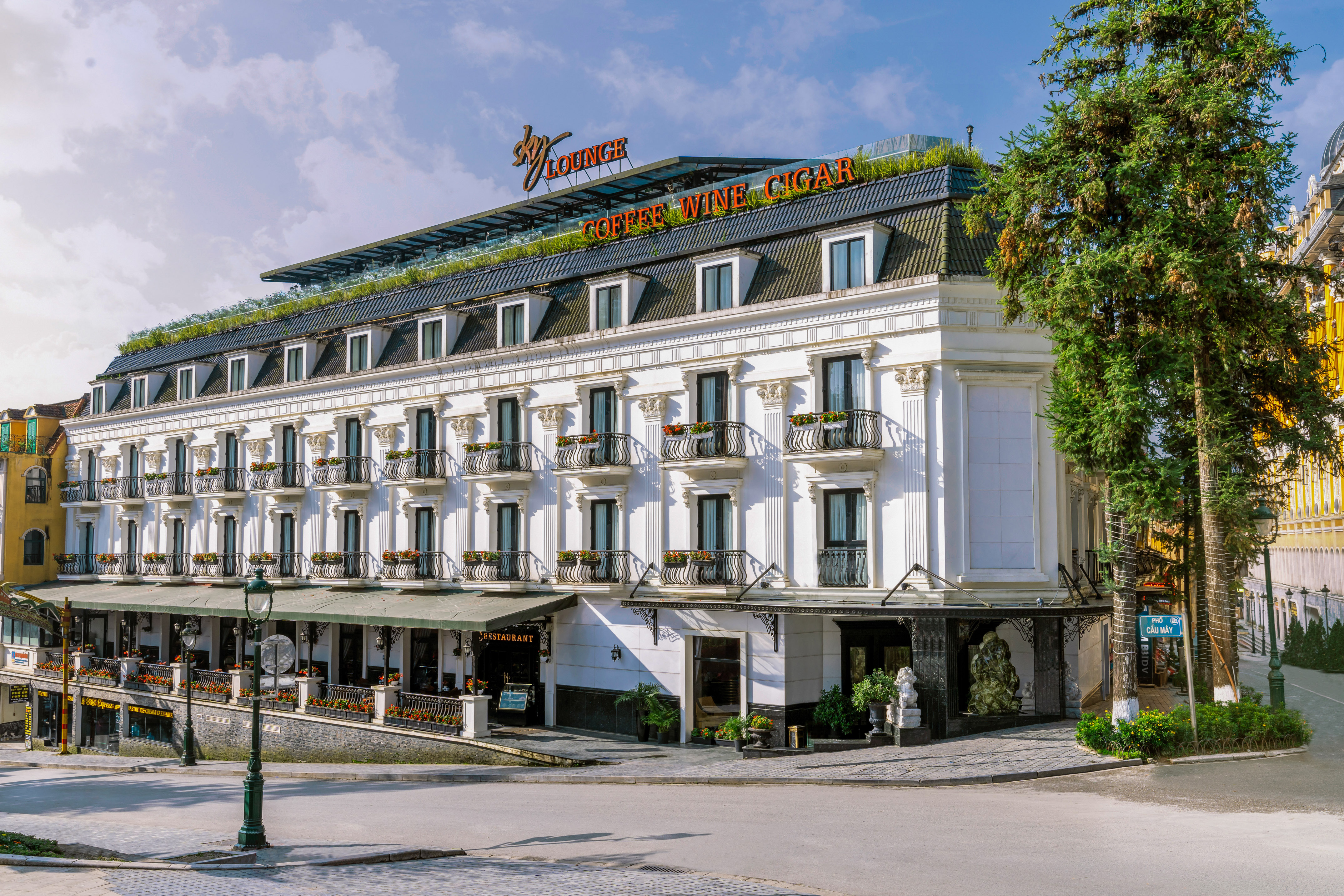 Elegant white hotel with balconies, rooftop lounge, and Coffee Wine Cigar.