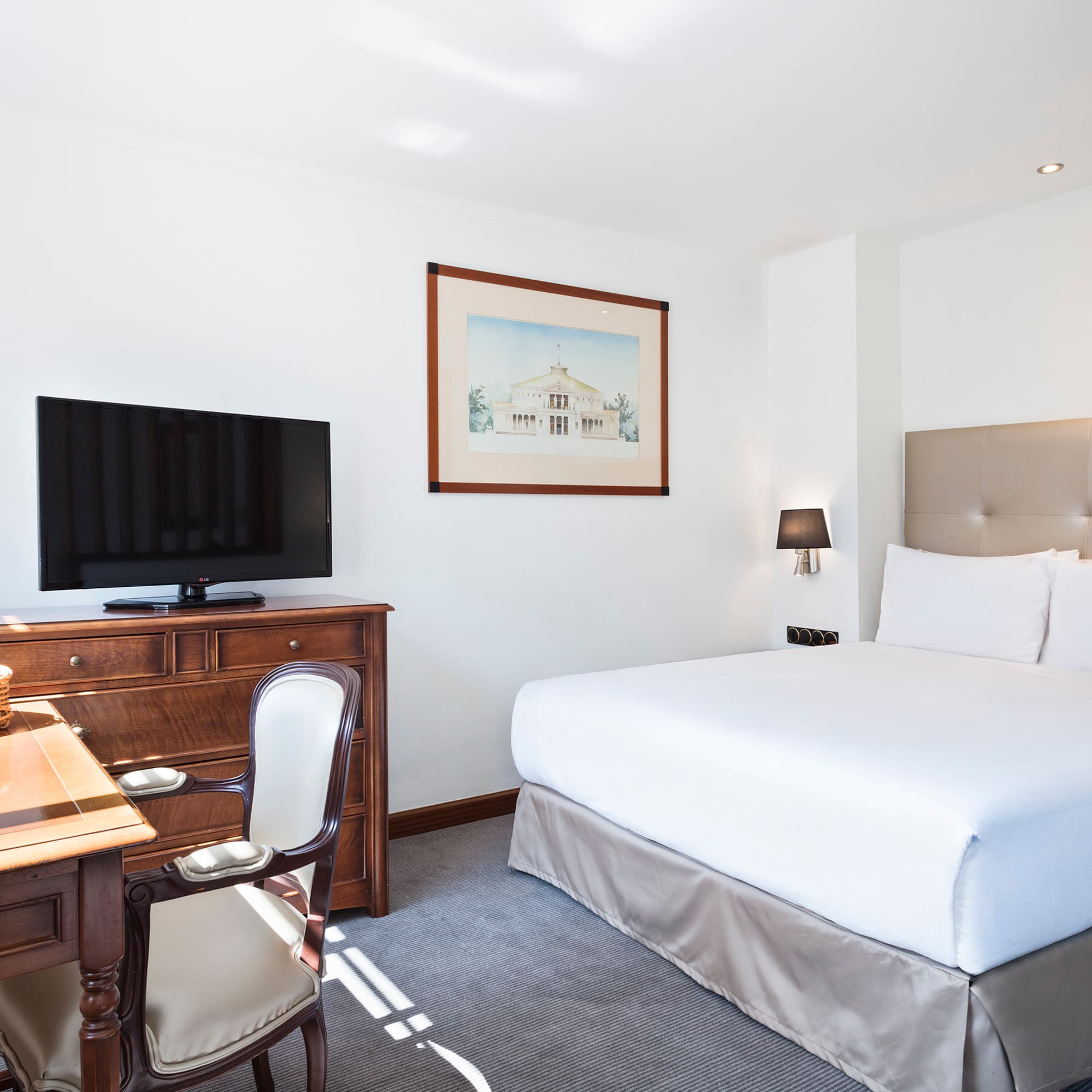 Bright hotel guest room with king bed, TV, wooden desk, and beige headboard.