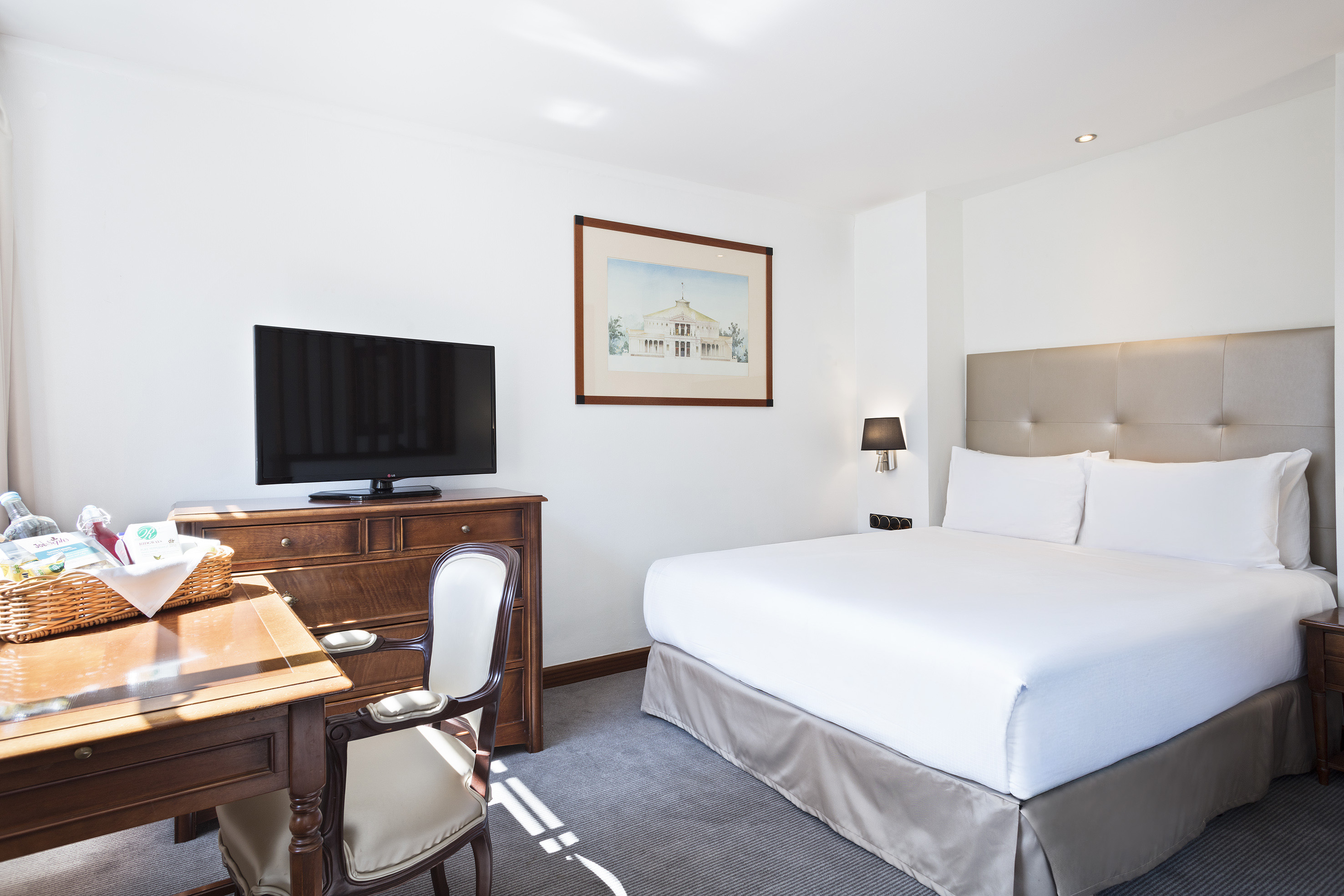 Bright hotel guest room with king bed, TV, wooden desk, and beige headboard.