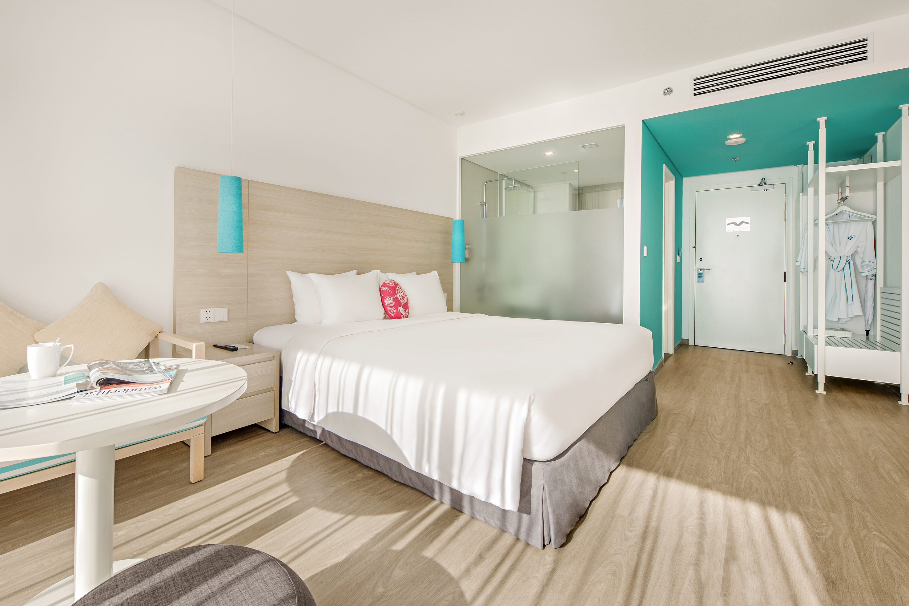 Modern hotel bedroom with king bed, white linens, wood floor, and turquoise accents.