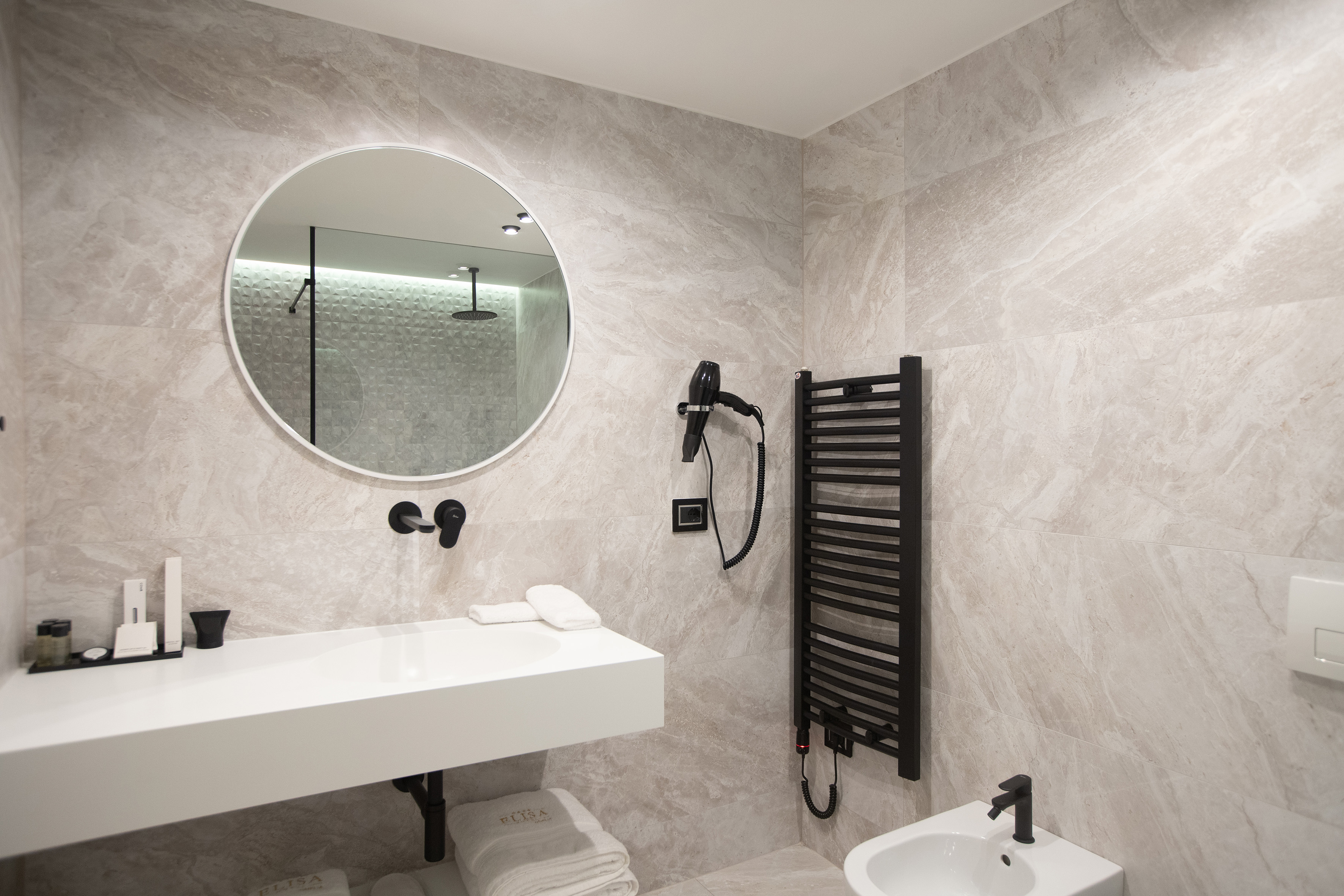 Modern gray tiled bathroom, white vanity, round mirror, black towel rail.