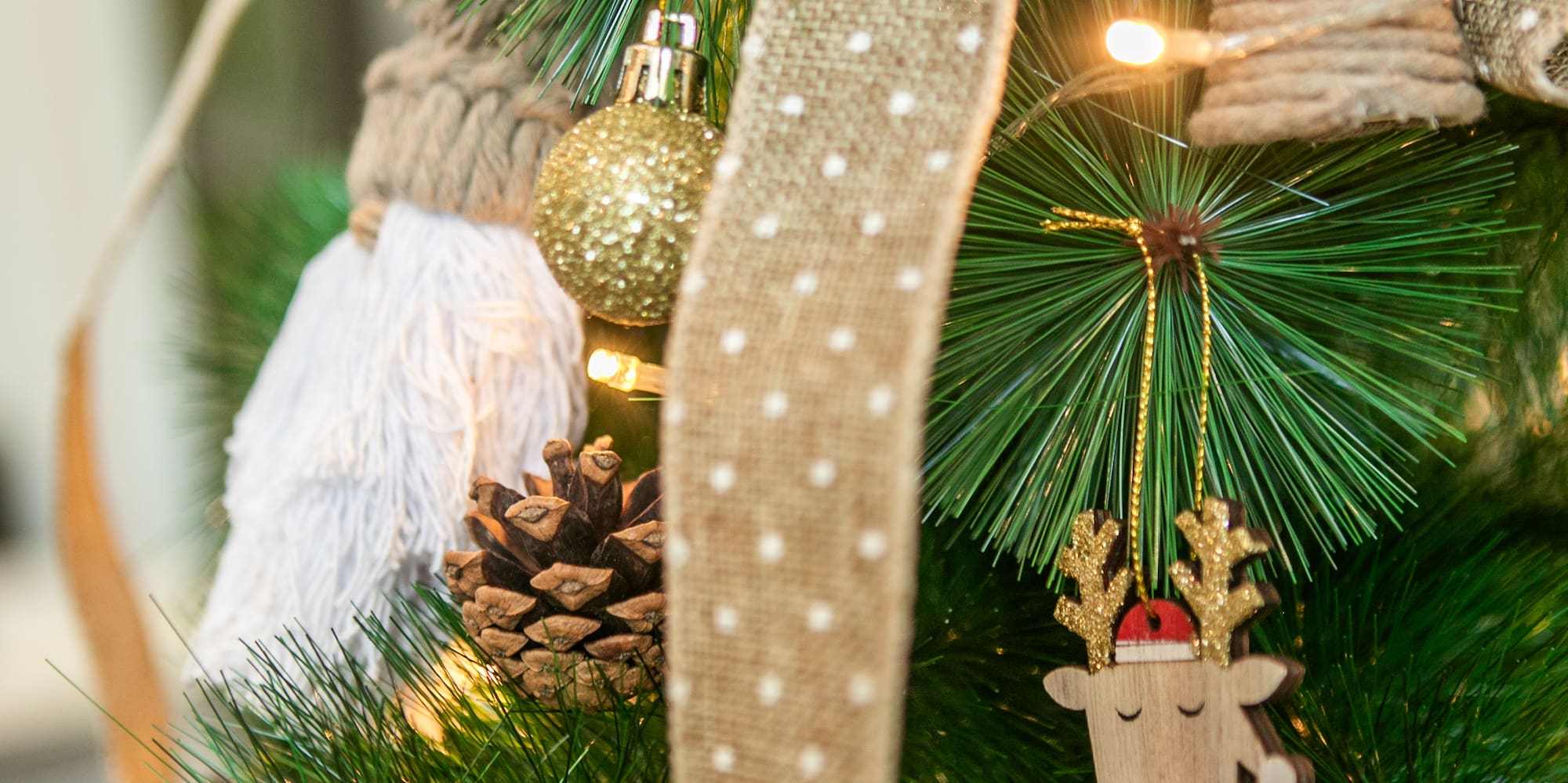 Christmas tree with burlap ribbon, lights, reindeer, and pinecone.