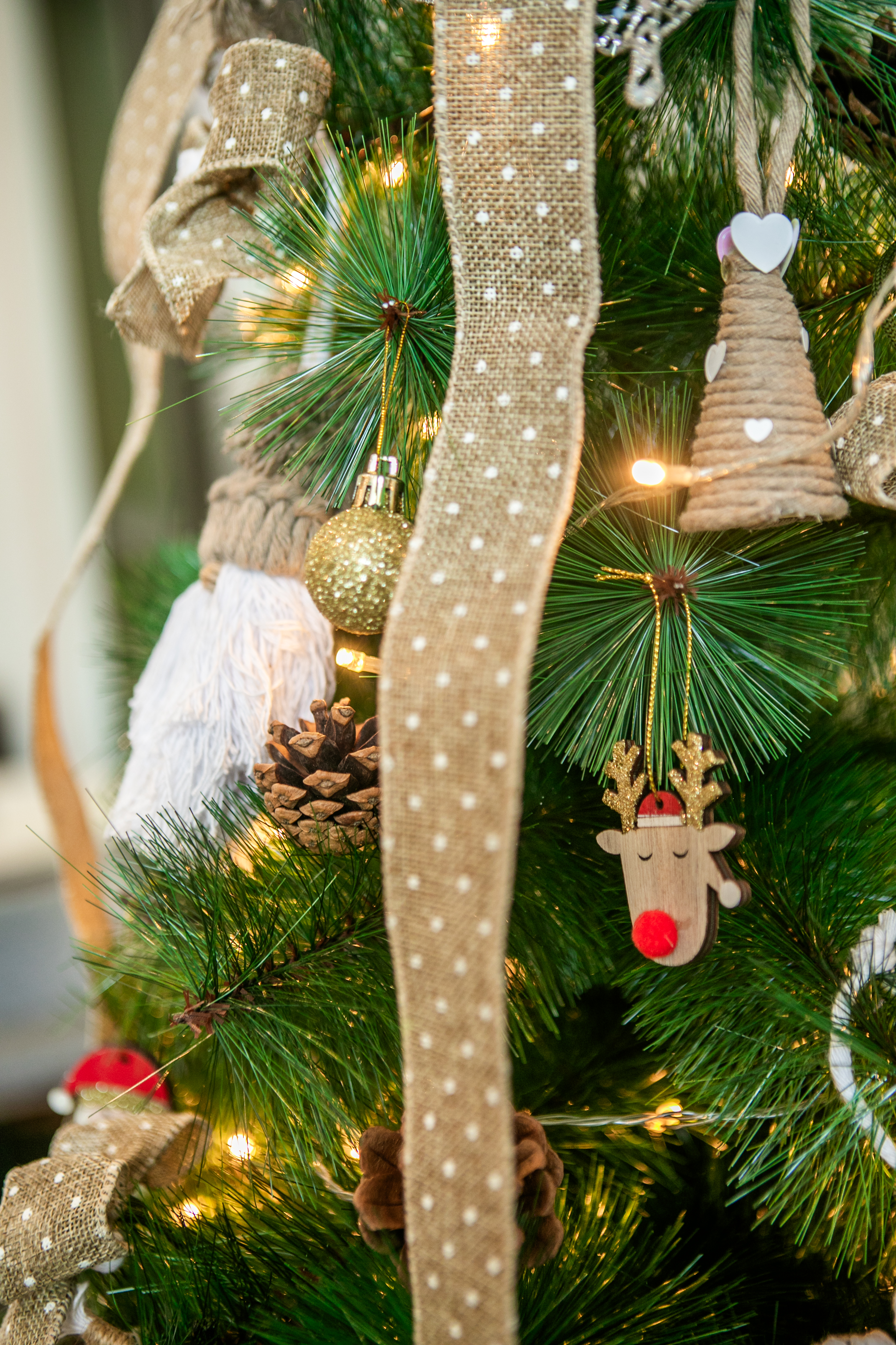 Christmas tree with burlap ribbon, lights, reindeer, and pinecone.