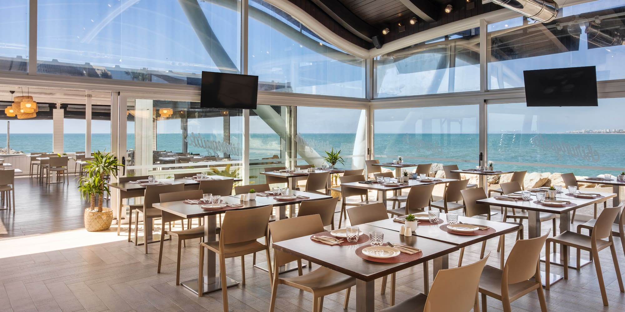 Modern oceanfront restaurant with set tables, large windows, and expansive sea view.