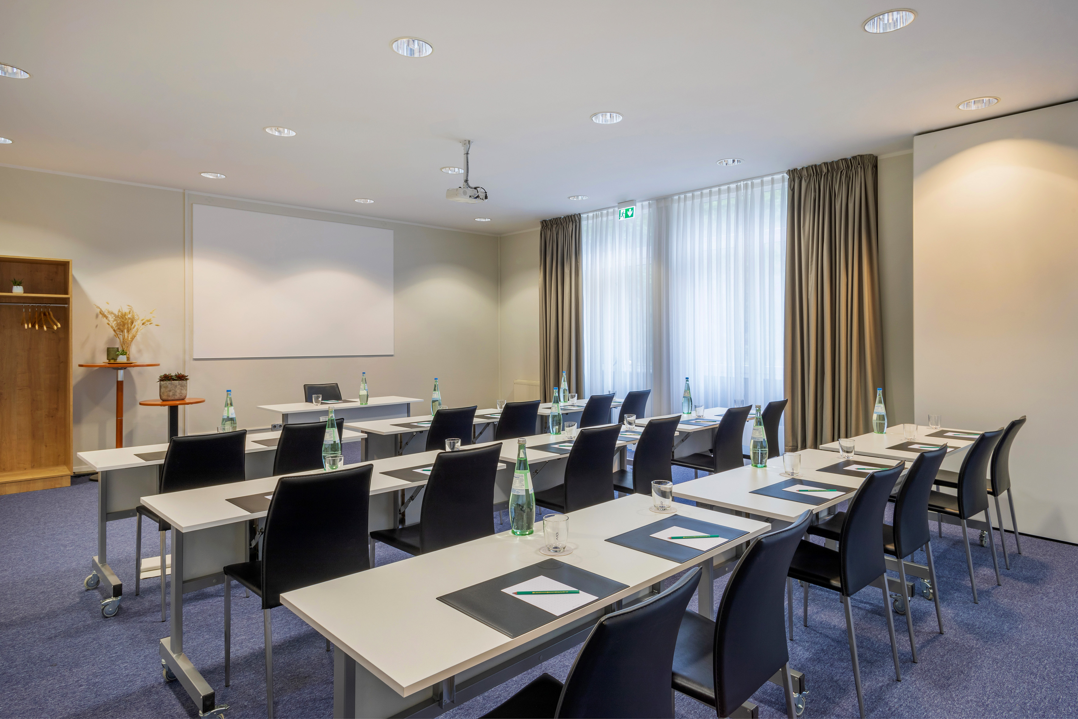 Classroom style conference room with projector, screen, tables, and chairs.