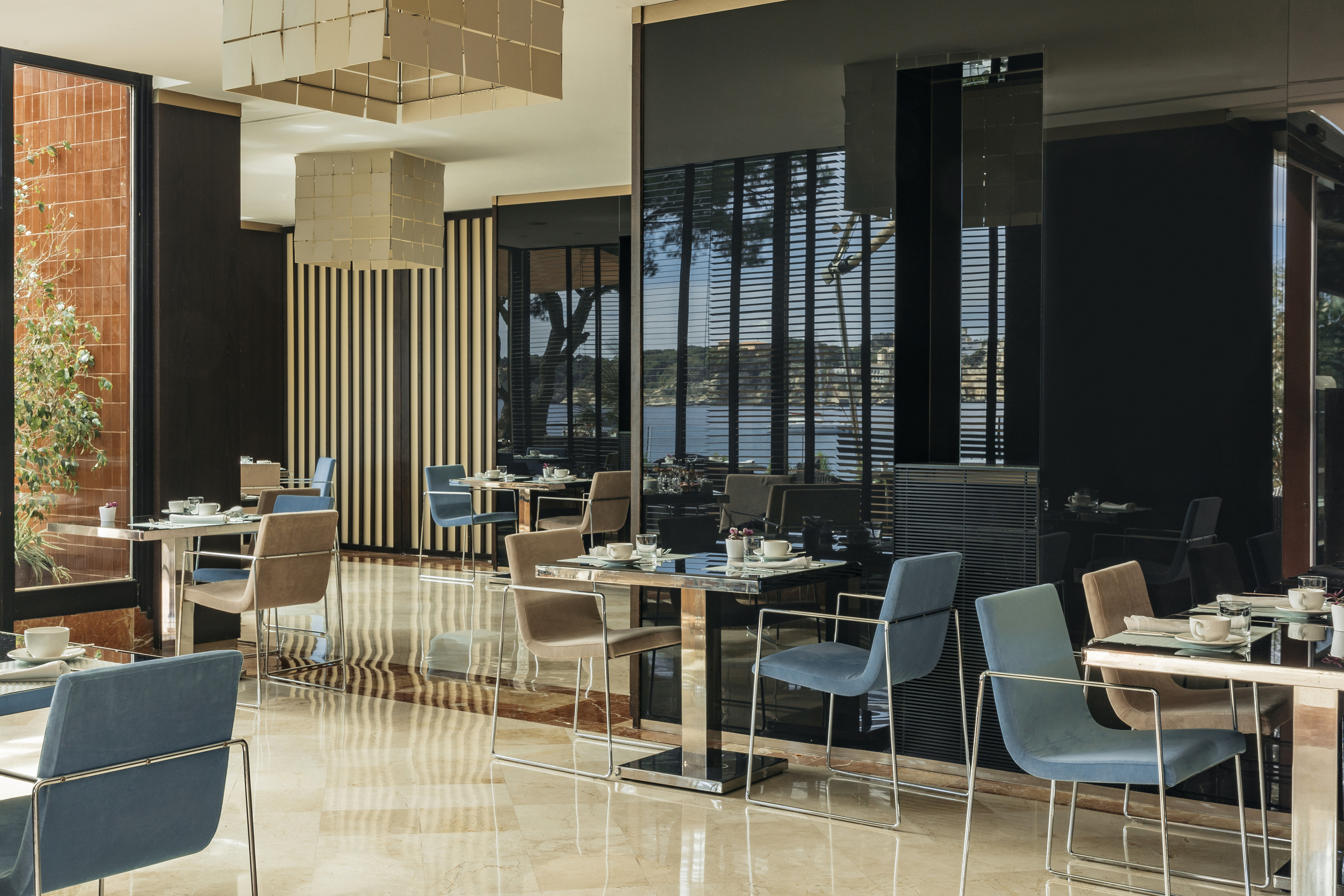 Modern hotel dining room with set tables, blue chairs, and bay view.