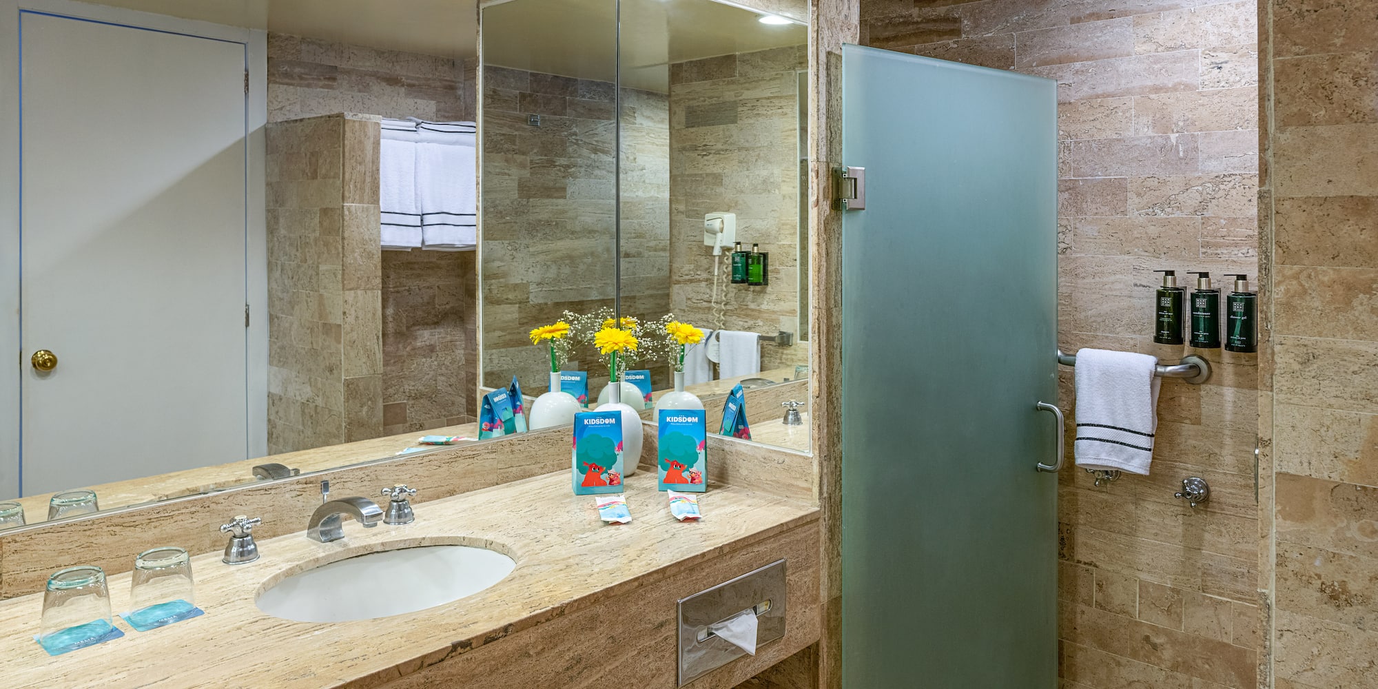 Modern hotel bathroom with marble vanity, large mirror, and frosted glass shower.