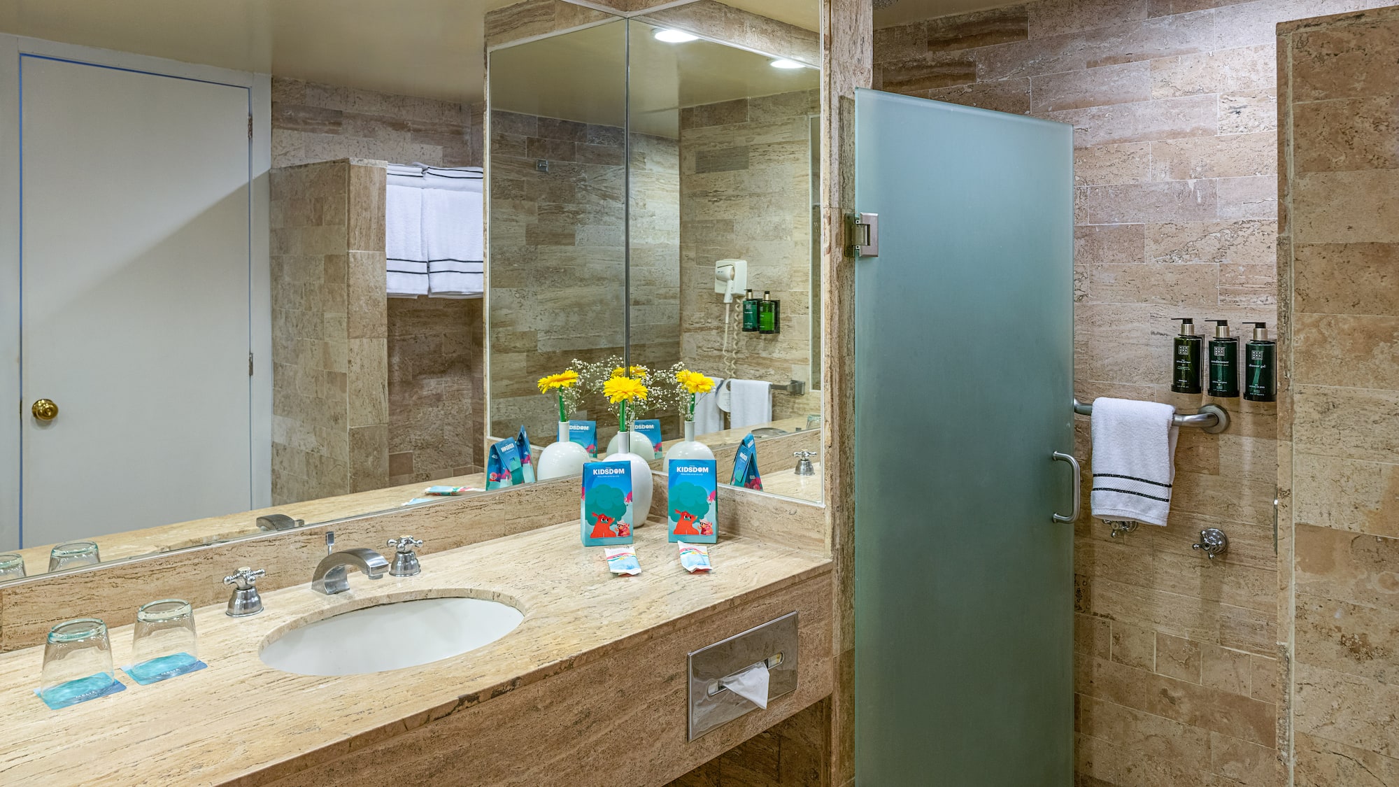 Hotel bathroom: stone vanity, basin, large mirror, frosted glass shower.