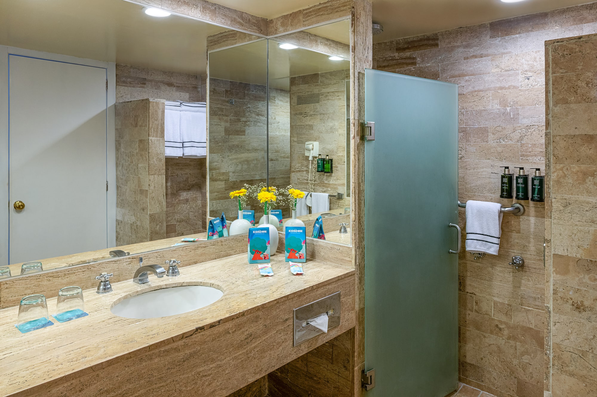 Modern hotel bathroom with marble vanity, large mirror, and frosted glass shower.