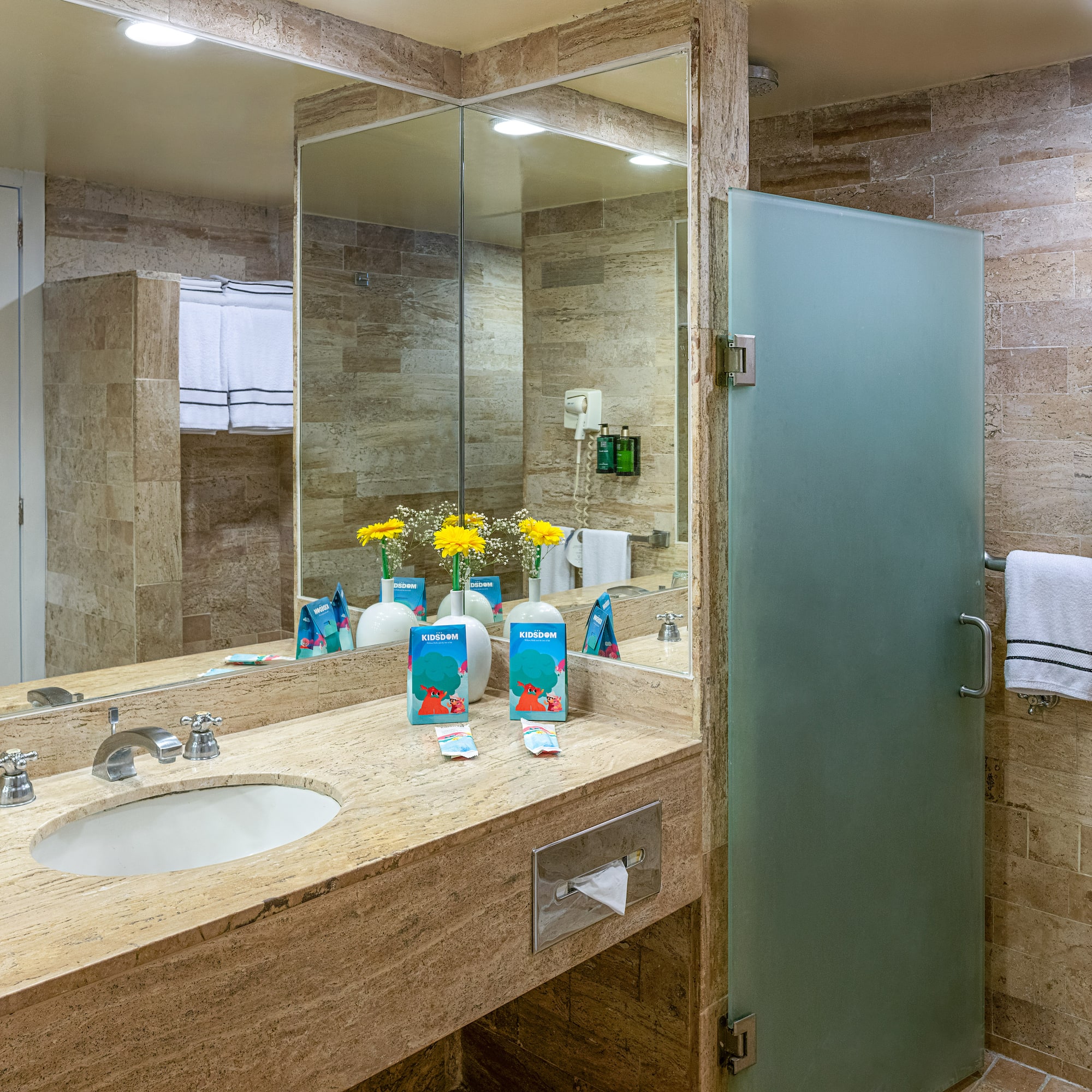 Hotel bathroom: stone vanity, basin, large mirror, frosted glass shower.