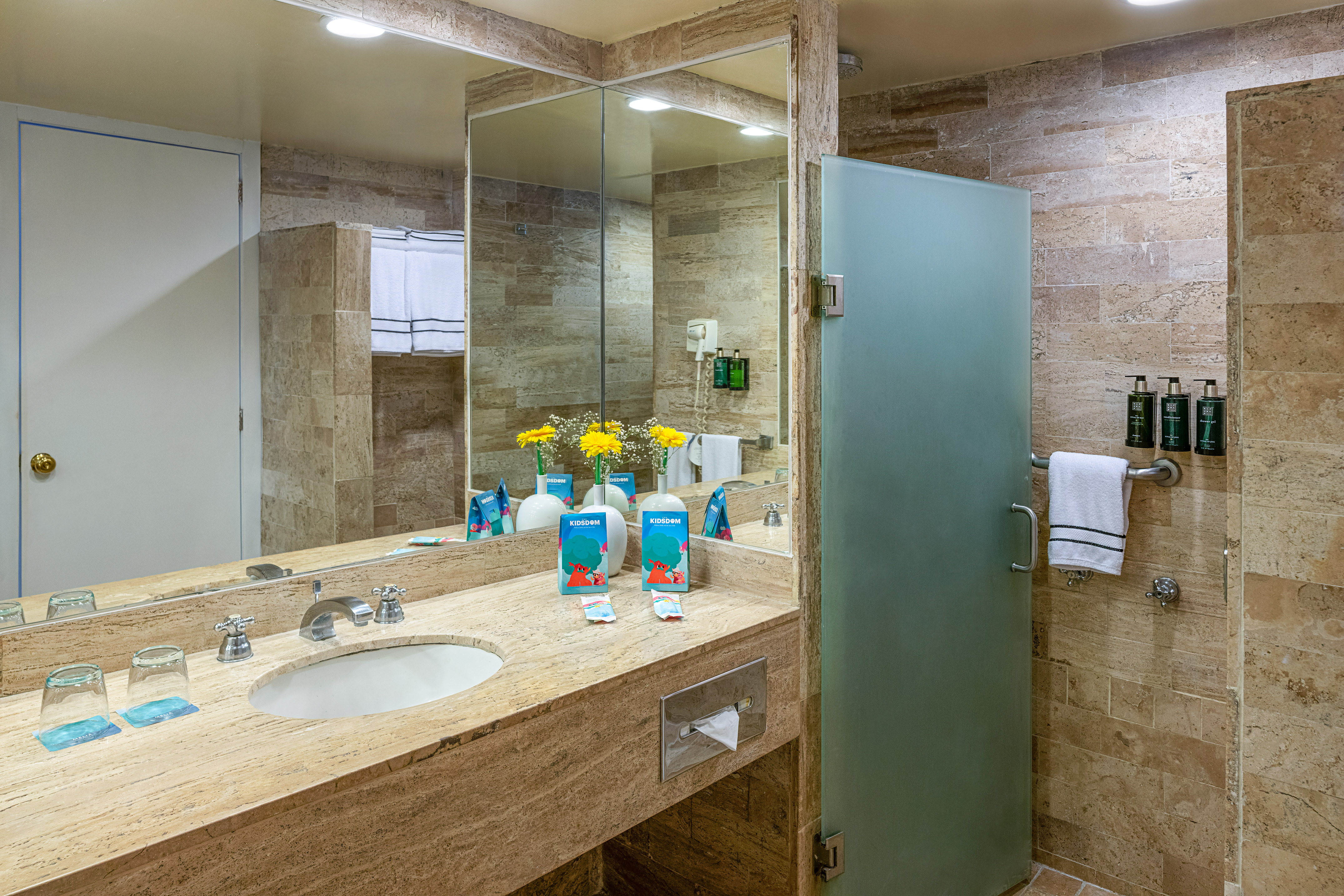 Modern hotel bathroom with marble vanity, large mirror, and frosted glass shower.