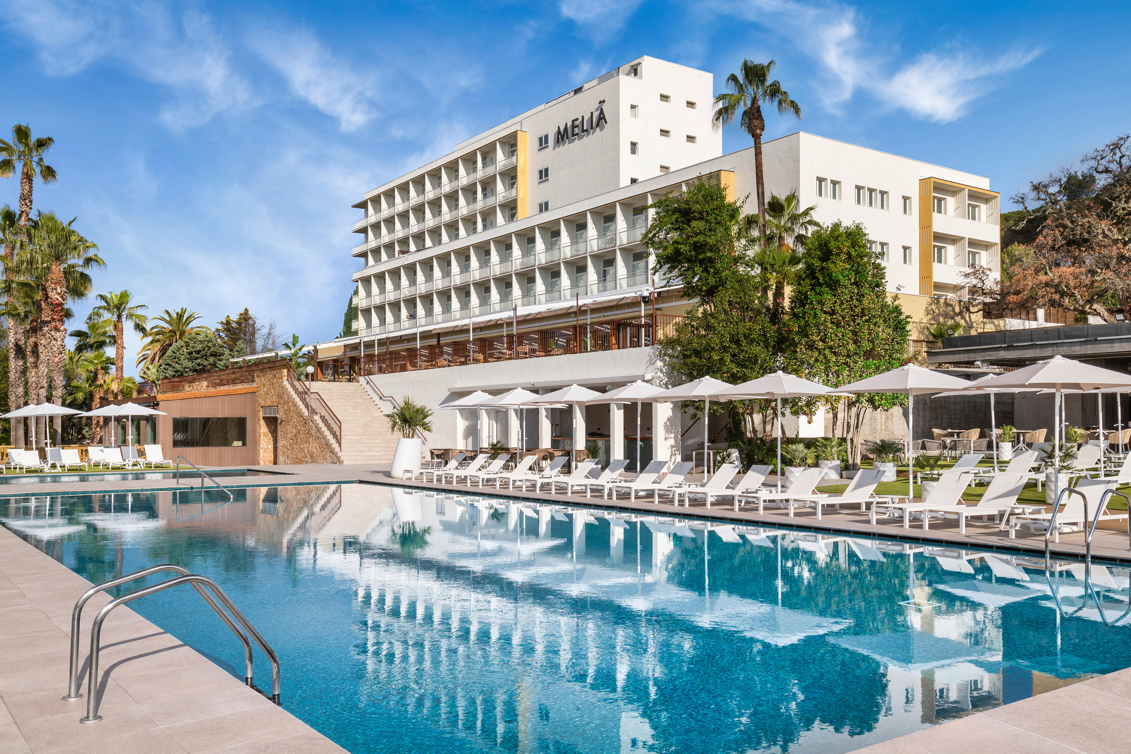 a pool with umbrellas and chairs in front of a building.