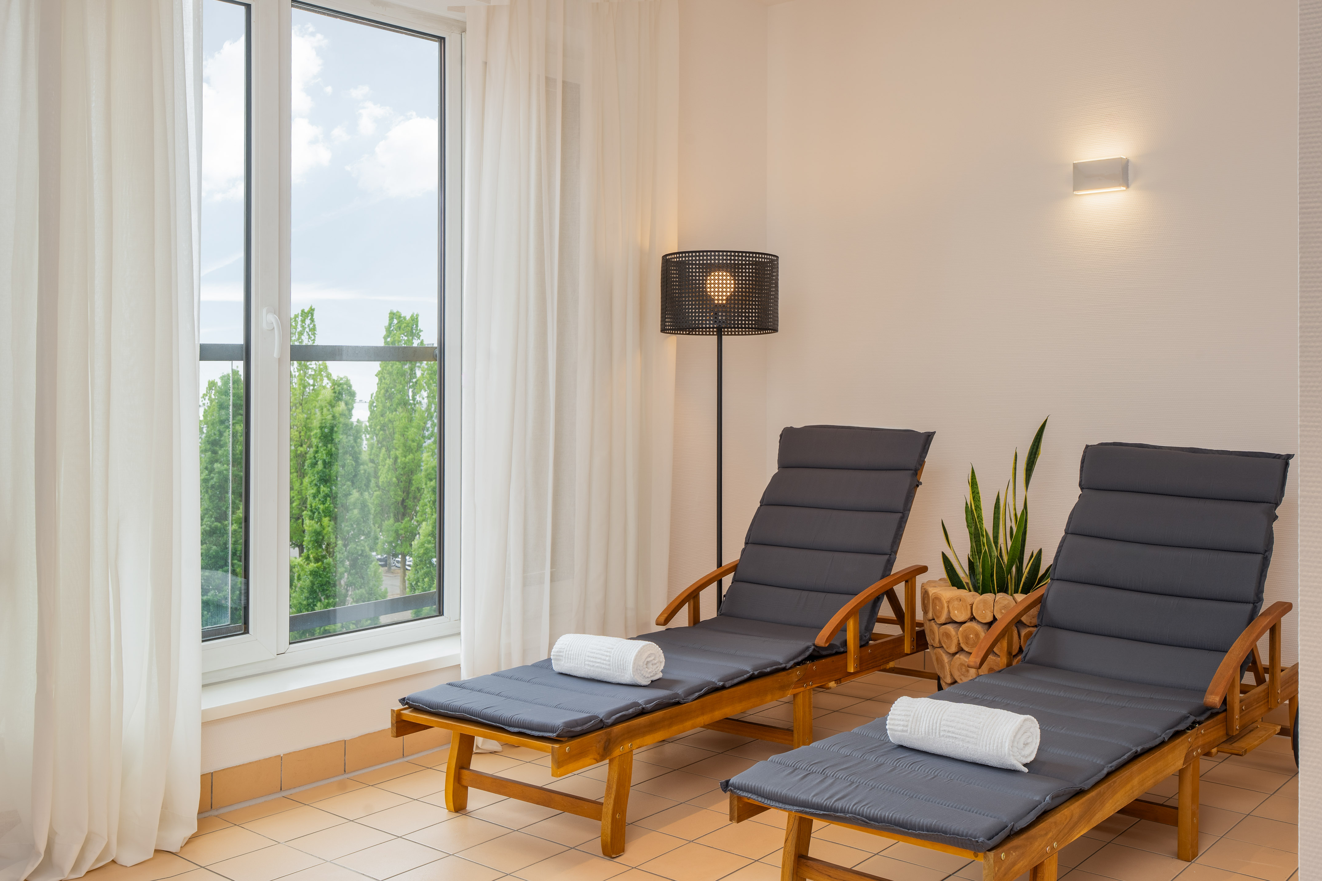 Indoor spa relaxation lounge with two lounge chairs, towels, and window view.