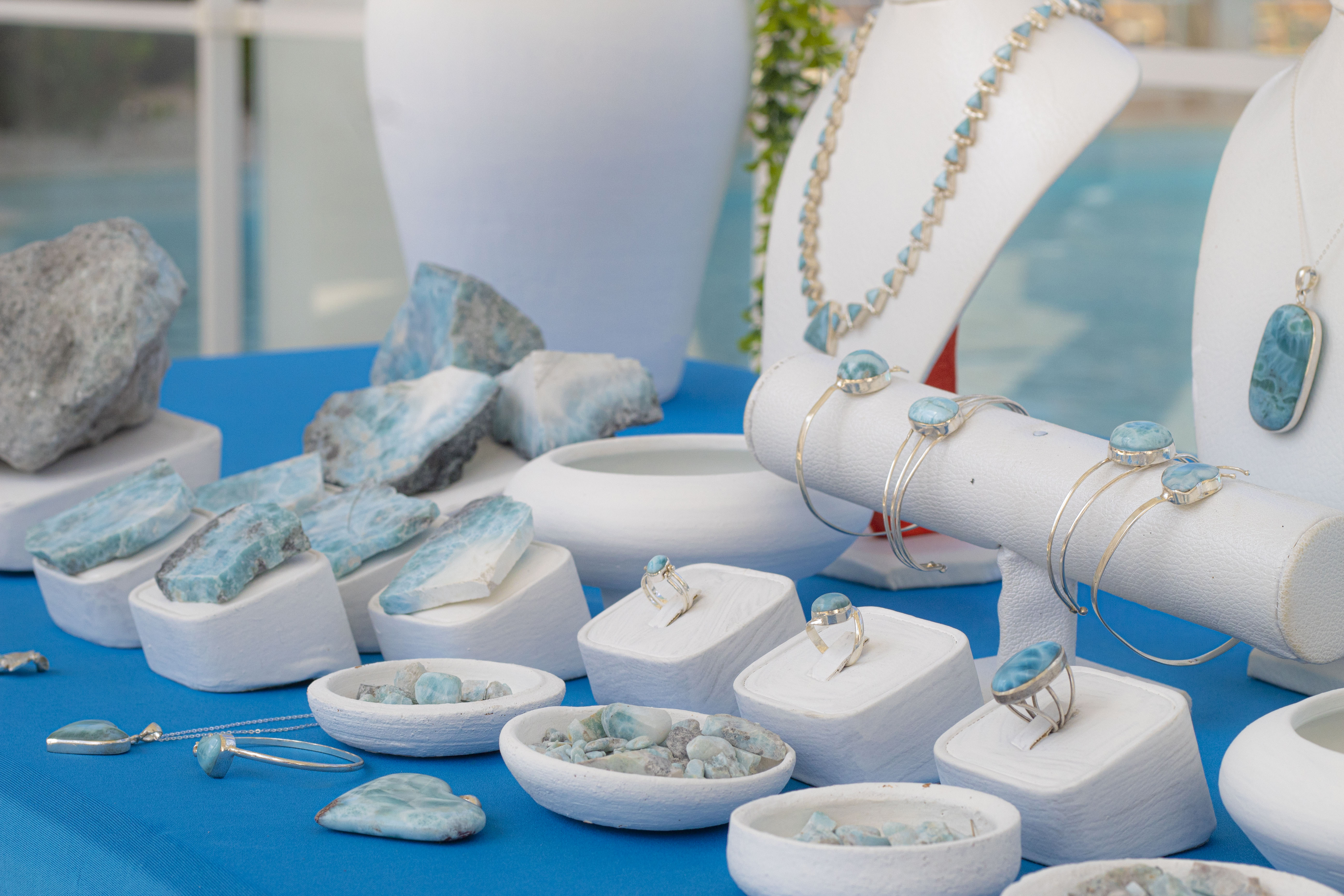 Larimar gemstone jewelry and raw stones displayed on a blue table.