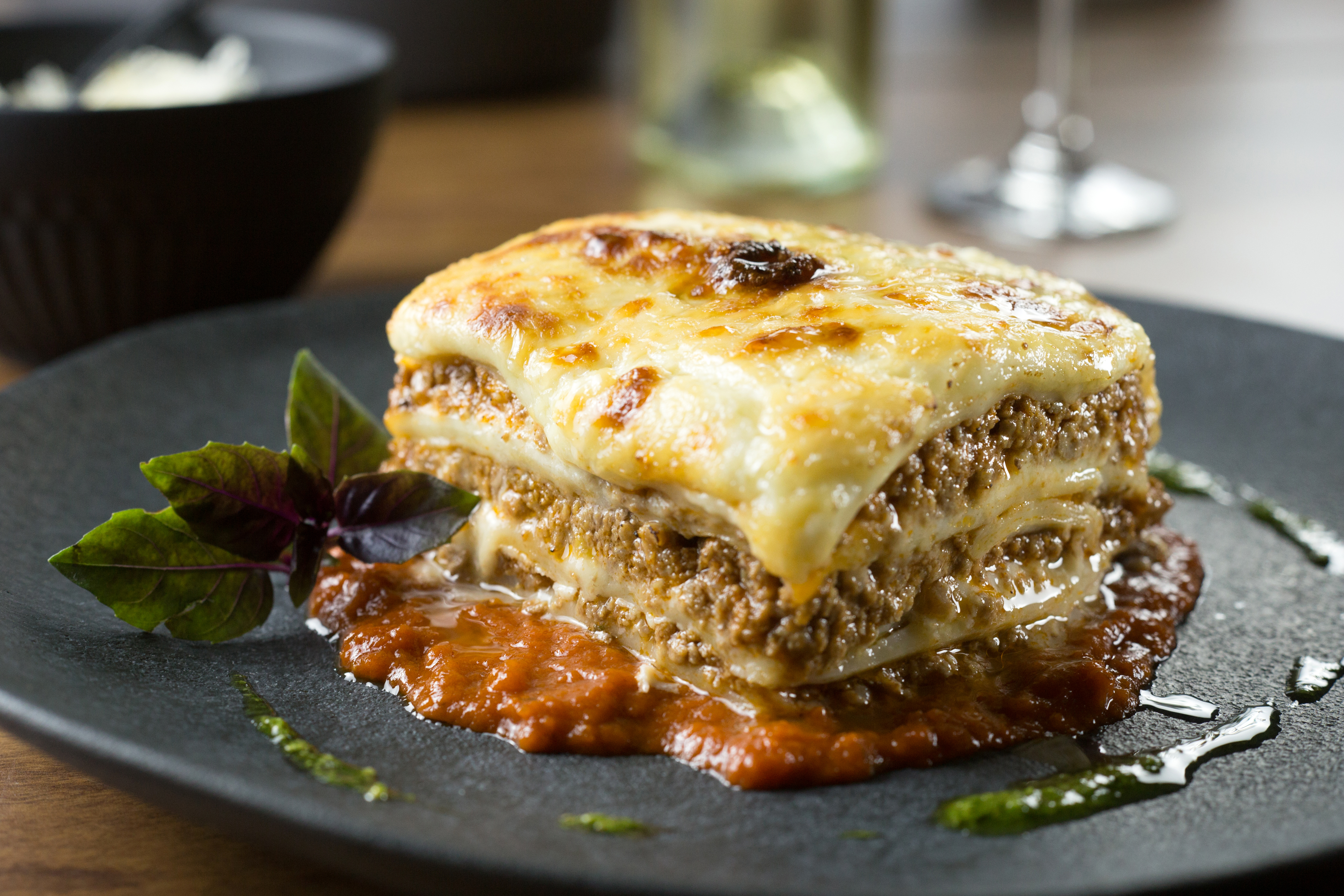 Baked lasagna with melted cheese, meat sauce, and fresh basil on dark plate.