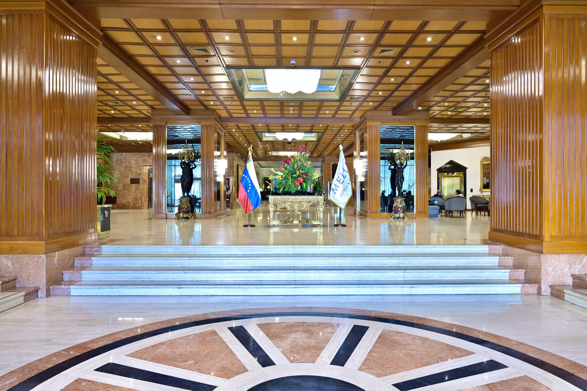 Grand hotel lobby with intricate wood paneling, patterned marble floor, and steps.
