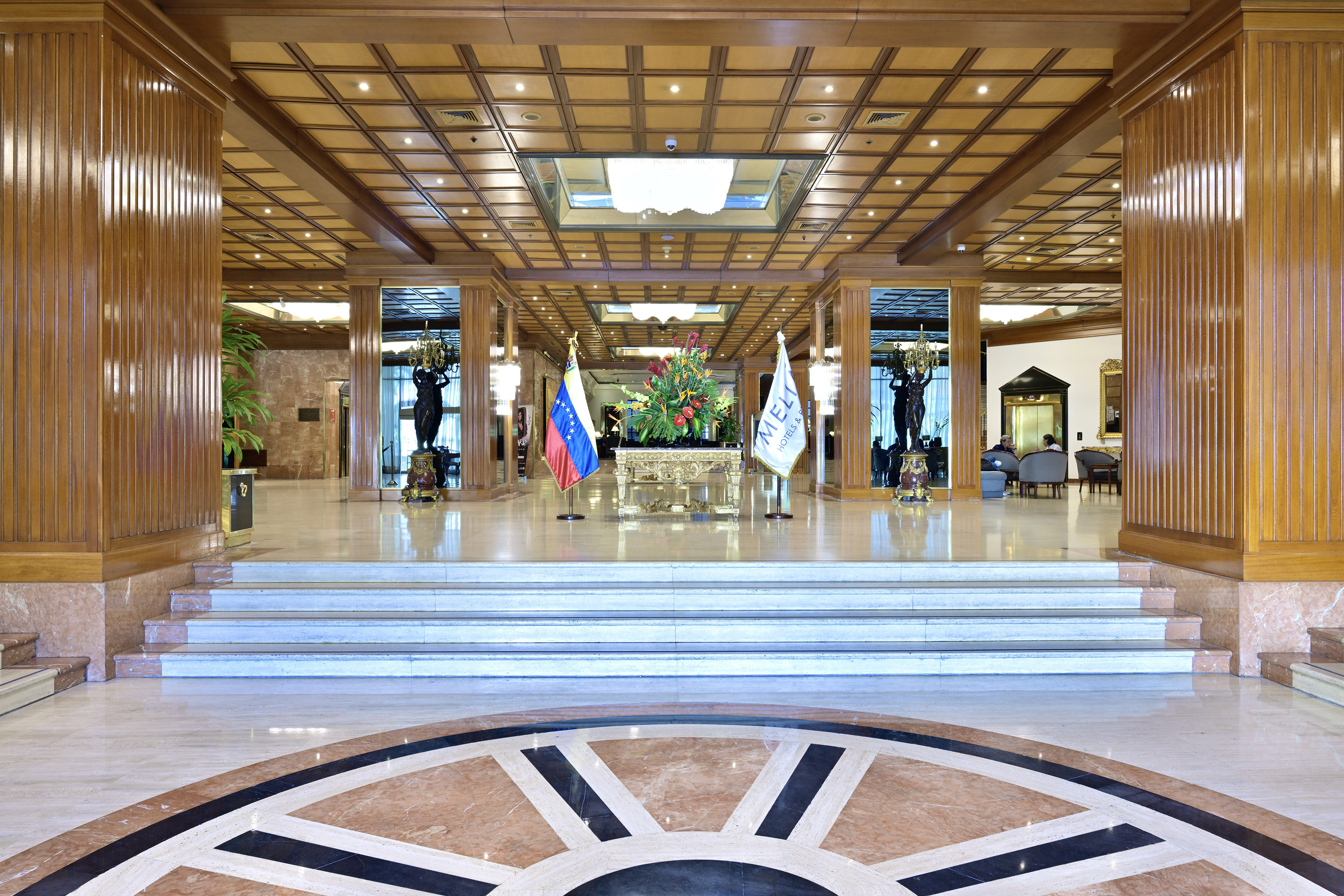 Grand hotel lobby with intricate wood paneling, patterned marble floor, and steps.